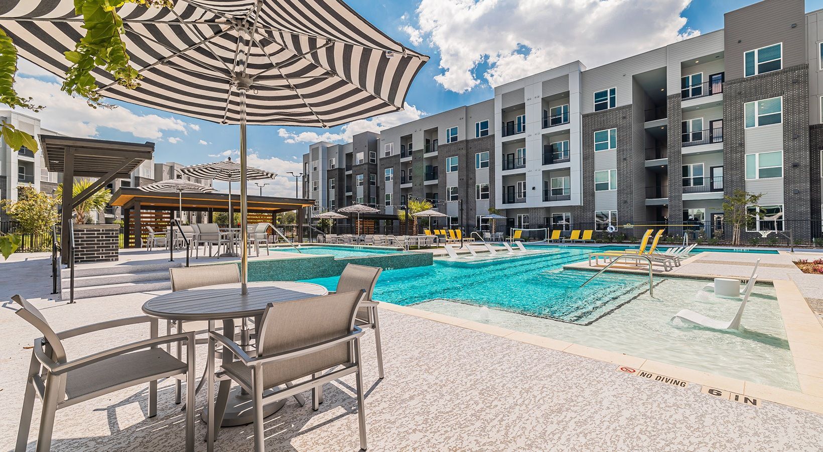 Modern apartment pool courtyard with loungers, umbrellas, and turquoise water under a striped canopy