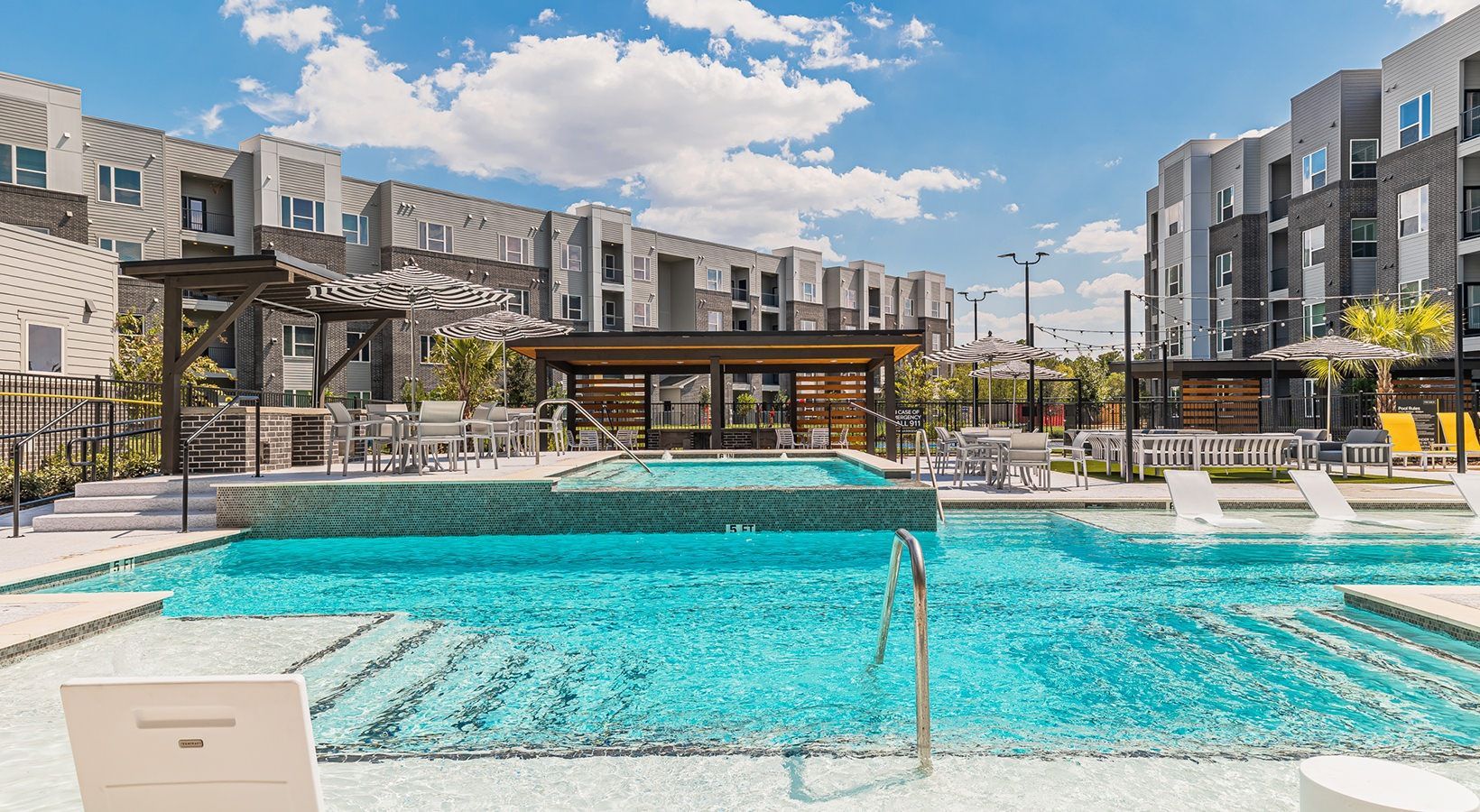 Modern apartment pool with turquoise water, lounge chairs, and a sunny courtyard backdrop