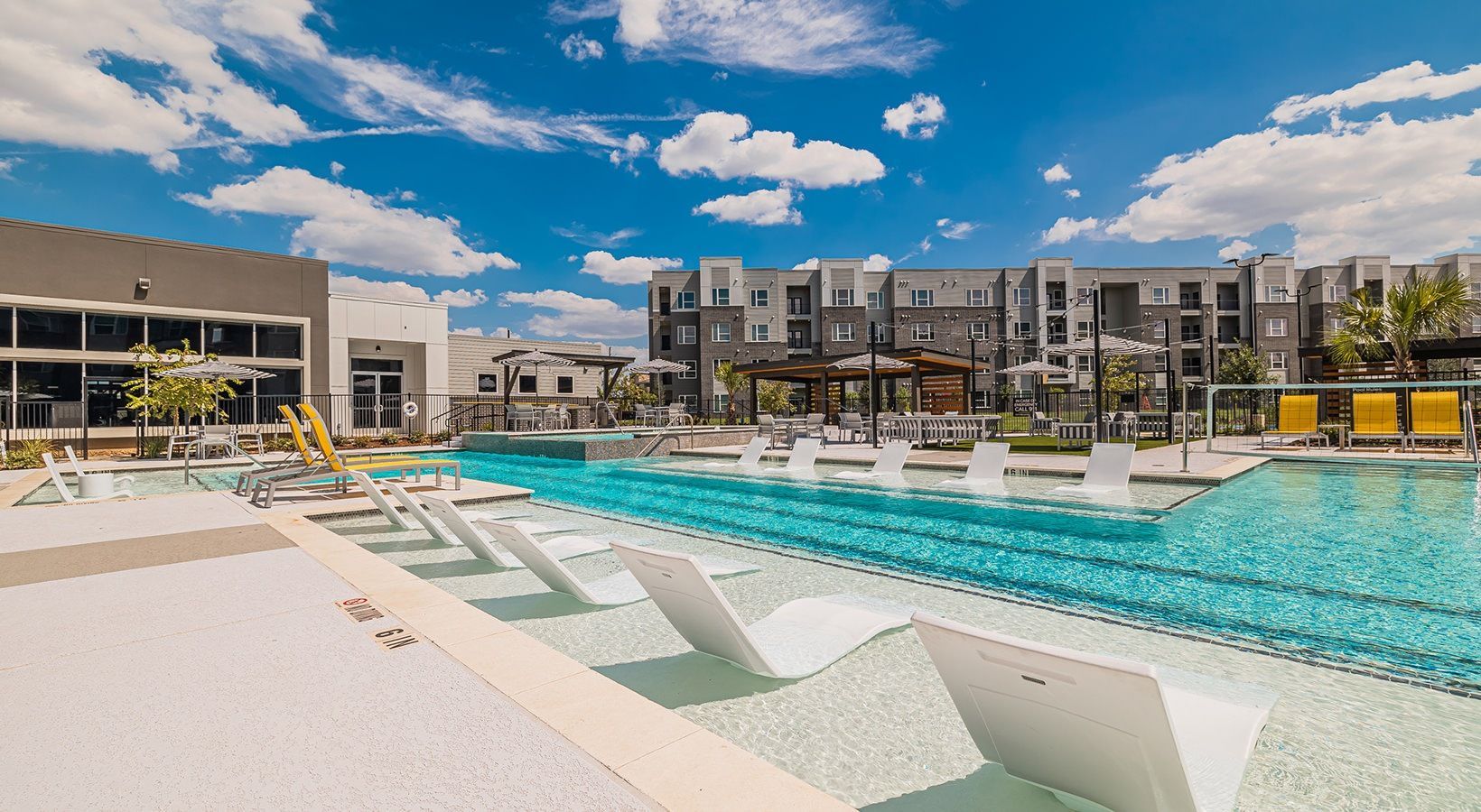 Modern apartment pool area with turquoise water, white loungers, and blue sky