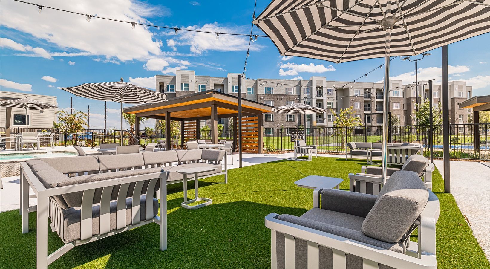 Rooftop terrace with white lounge chairs, striped umbrellas, green turf, and city buildings in the background