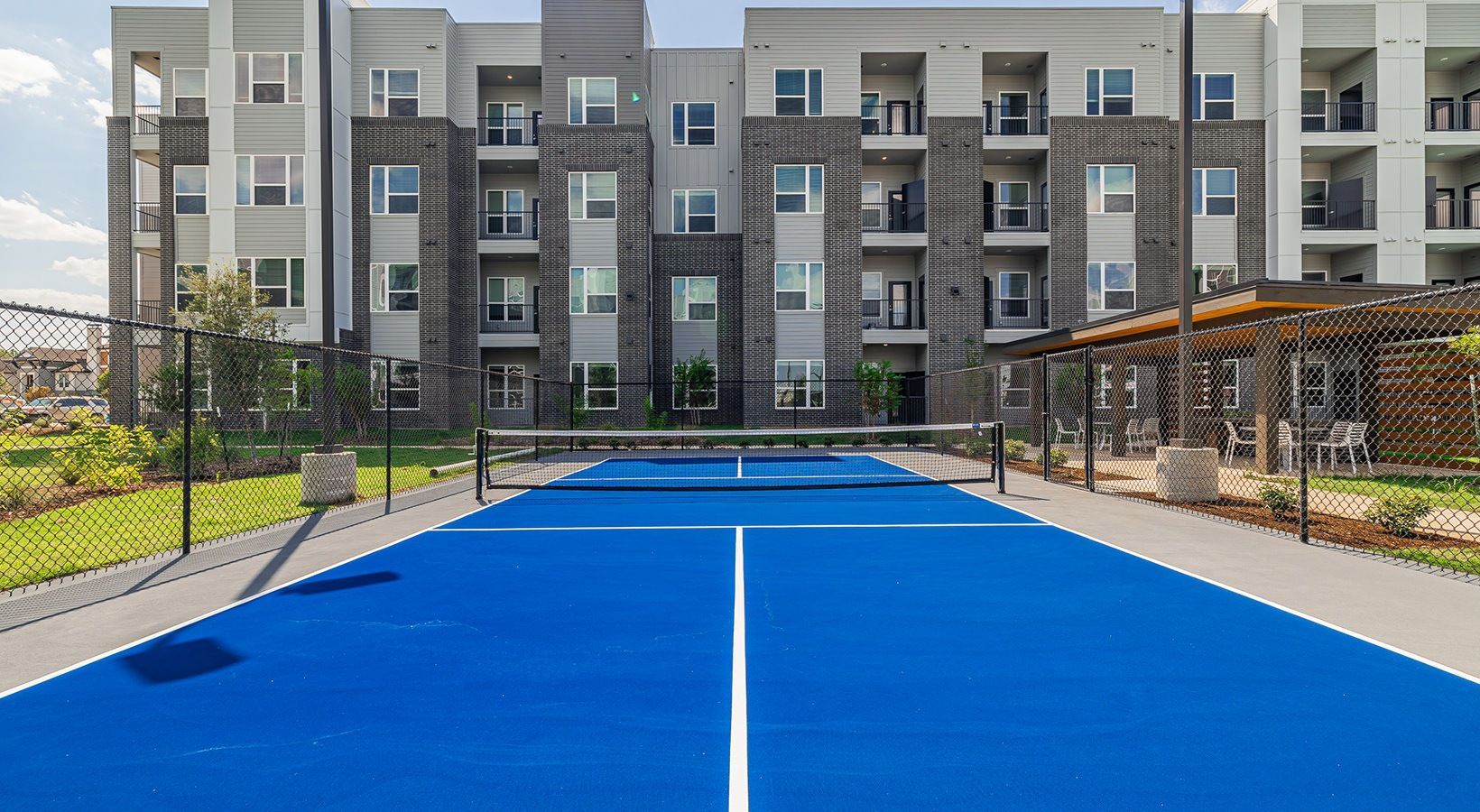 Blue pickleball court in an apartment complex courtyard with a modern building in the background