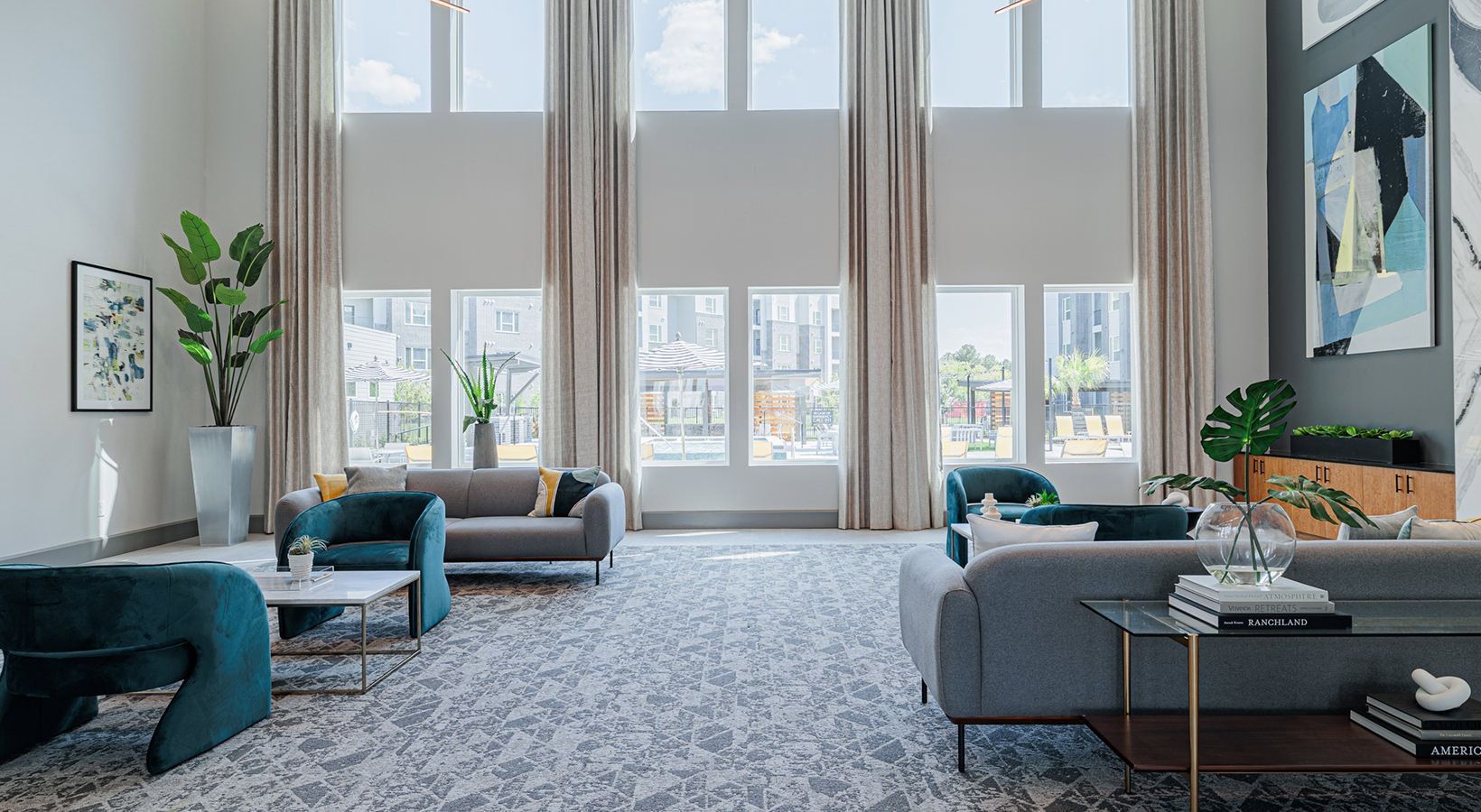 Modern living room with tall windows, gray sofas, teal chair, and patterned rug.