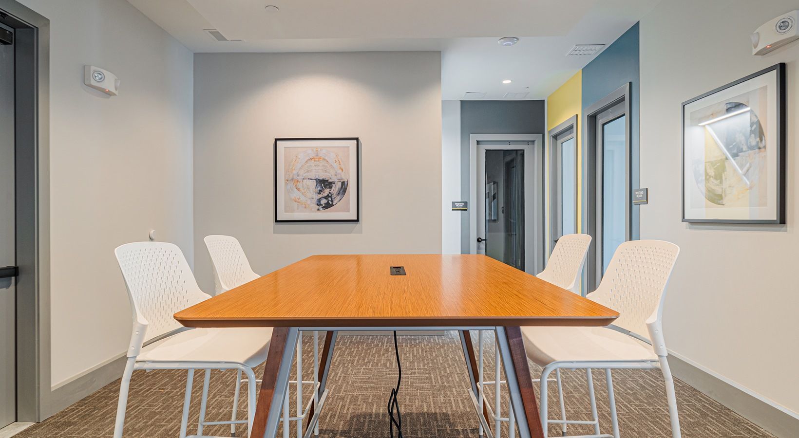 Modern conference room with a wooden table, white chairs, and framed wall art