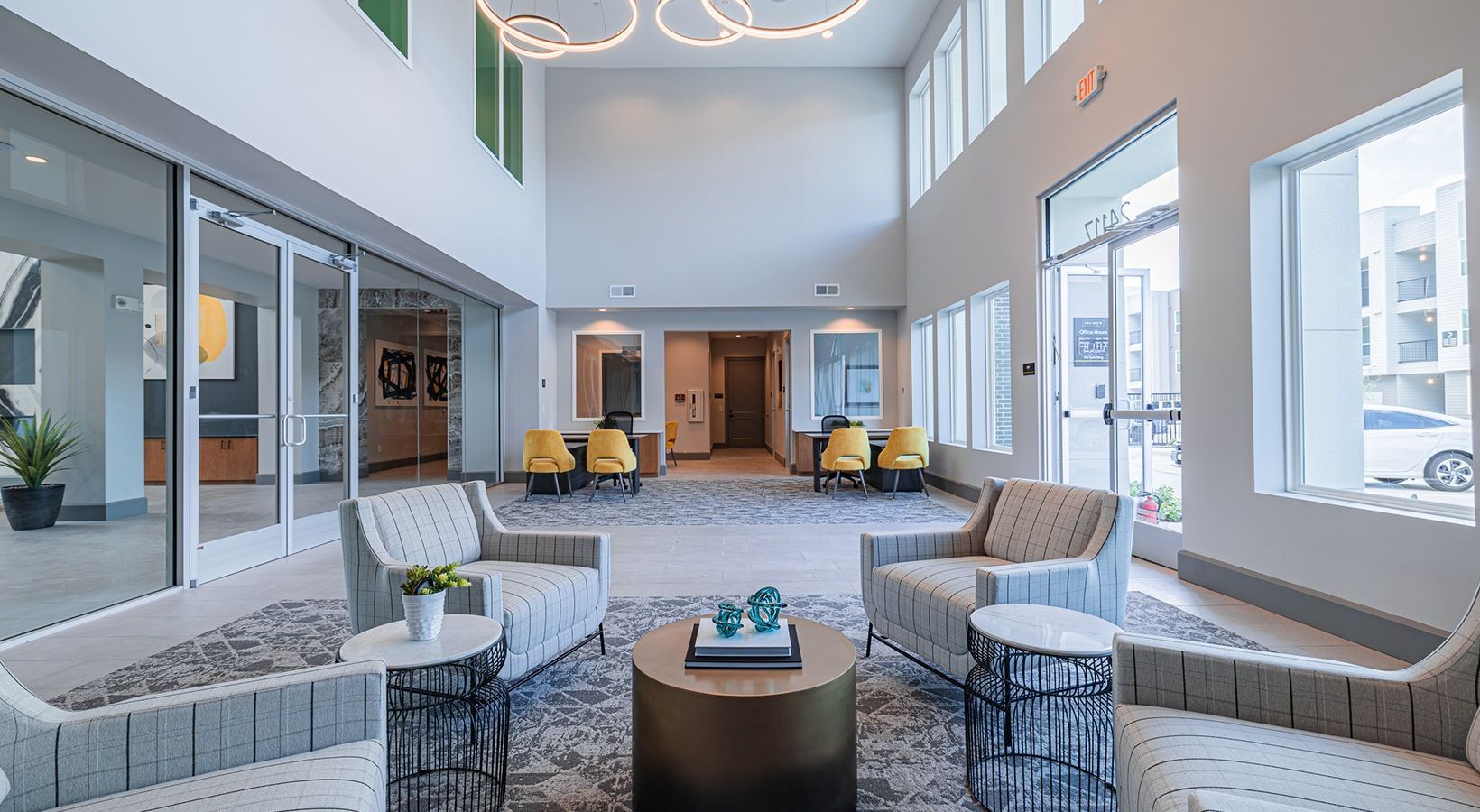 Bright modern lobby with white chairs, yellow accents, large windows, and a patterned rug