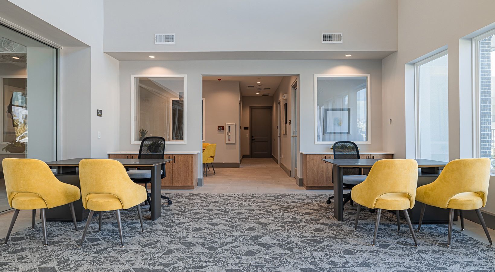 Modern office lobby with gray carpet, yellow chairs, desks, and hallway seating areas