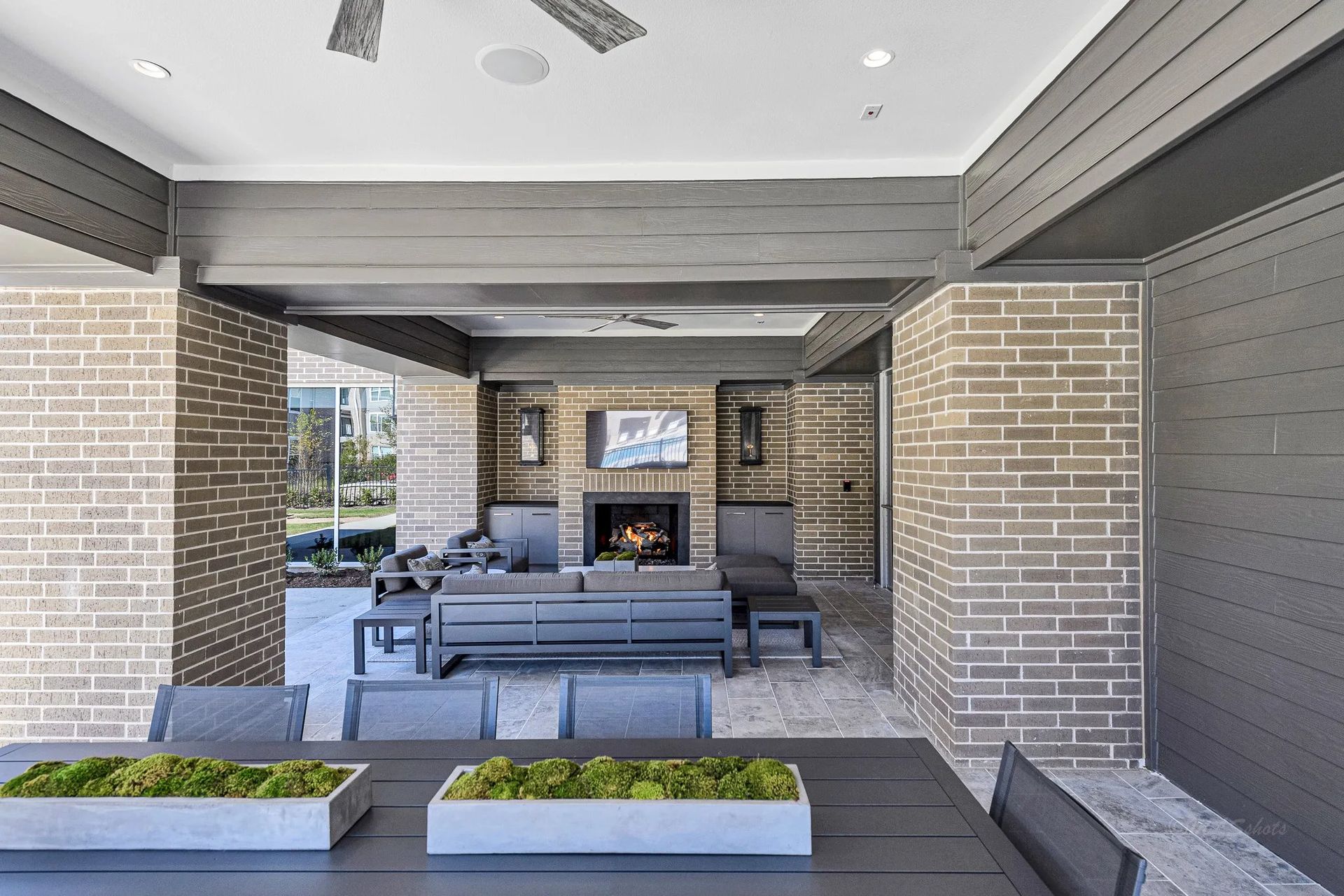 Covered outdoor patio with gray seating, brick columns, and a fireplace under a modern pergola