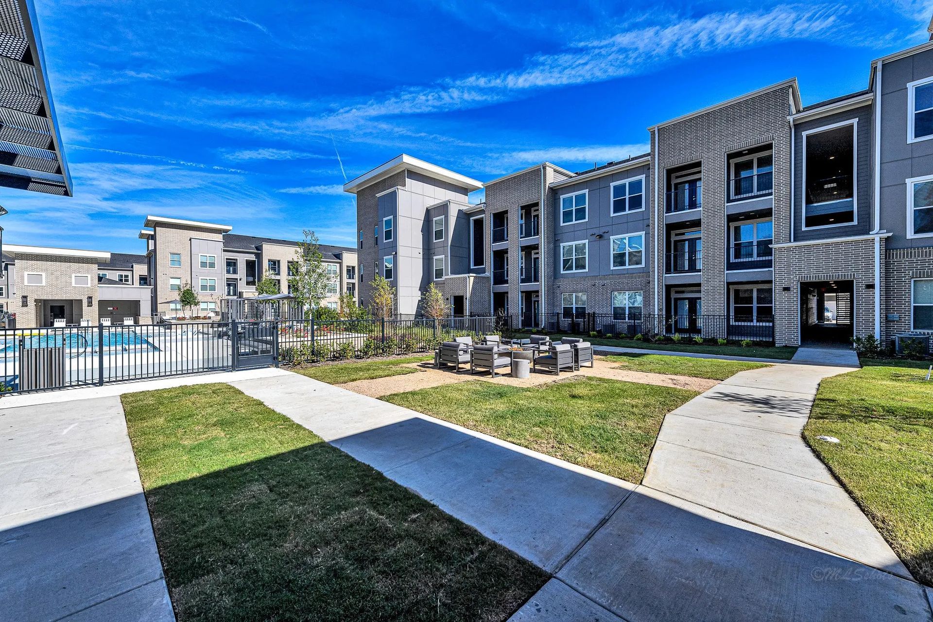 Modern apartment complex with a landscaped courtyard, walkways, and blue sky