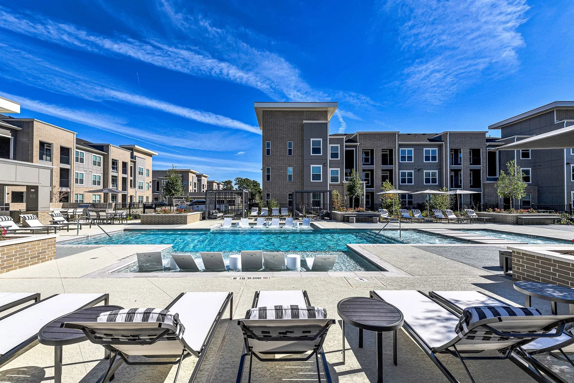 Modern apartment courtyard with empty pool, lounge chairs, and blue sky