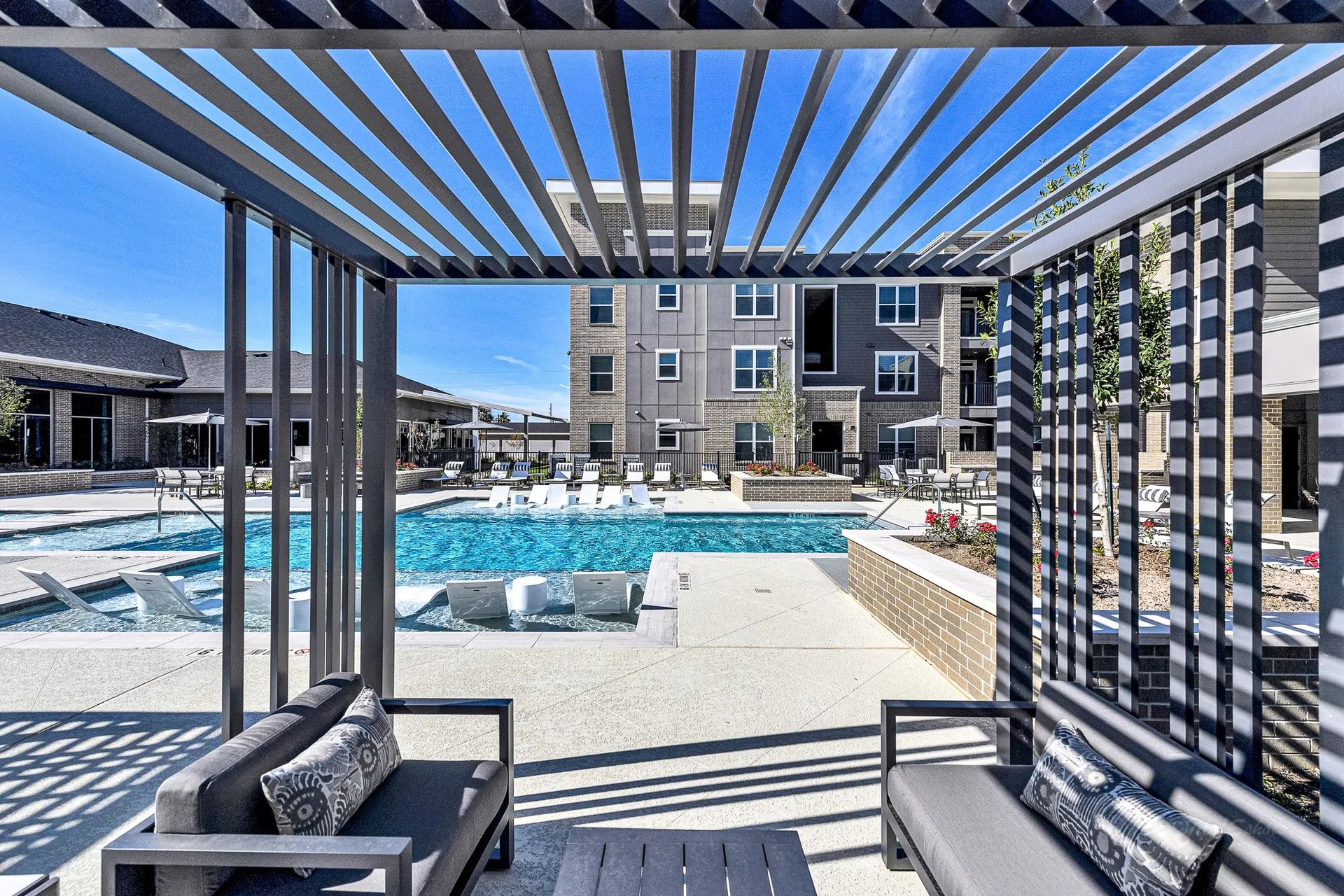 Poolside cabana with lounge chairs overlooking a bright resort pool and apartment buildings.