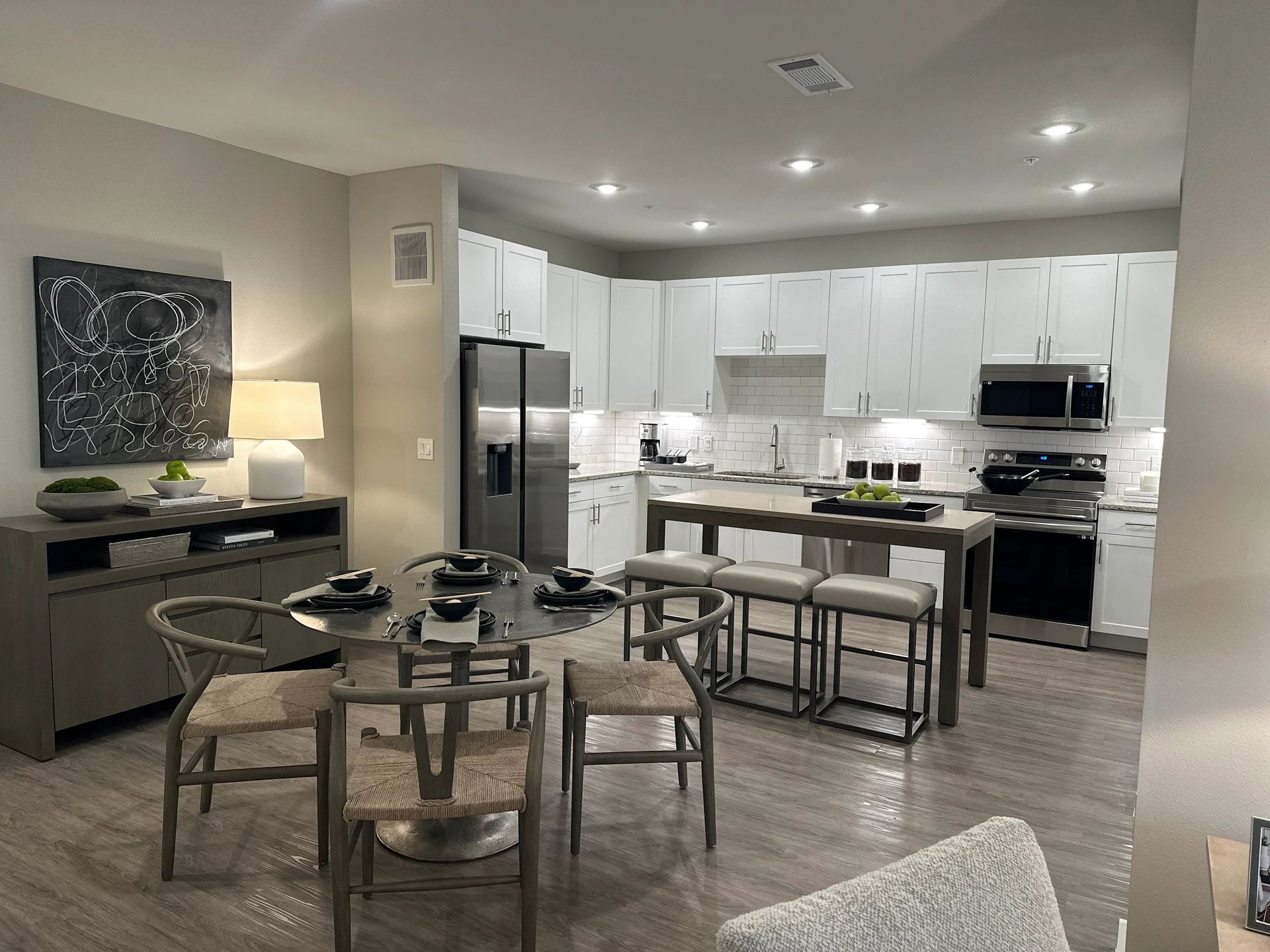 Modern open kitchen and dining area with white cabinets, gray tile, and a round table set for dining