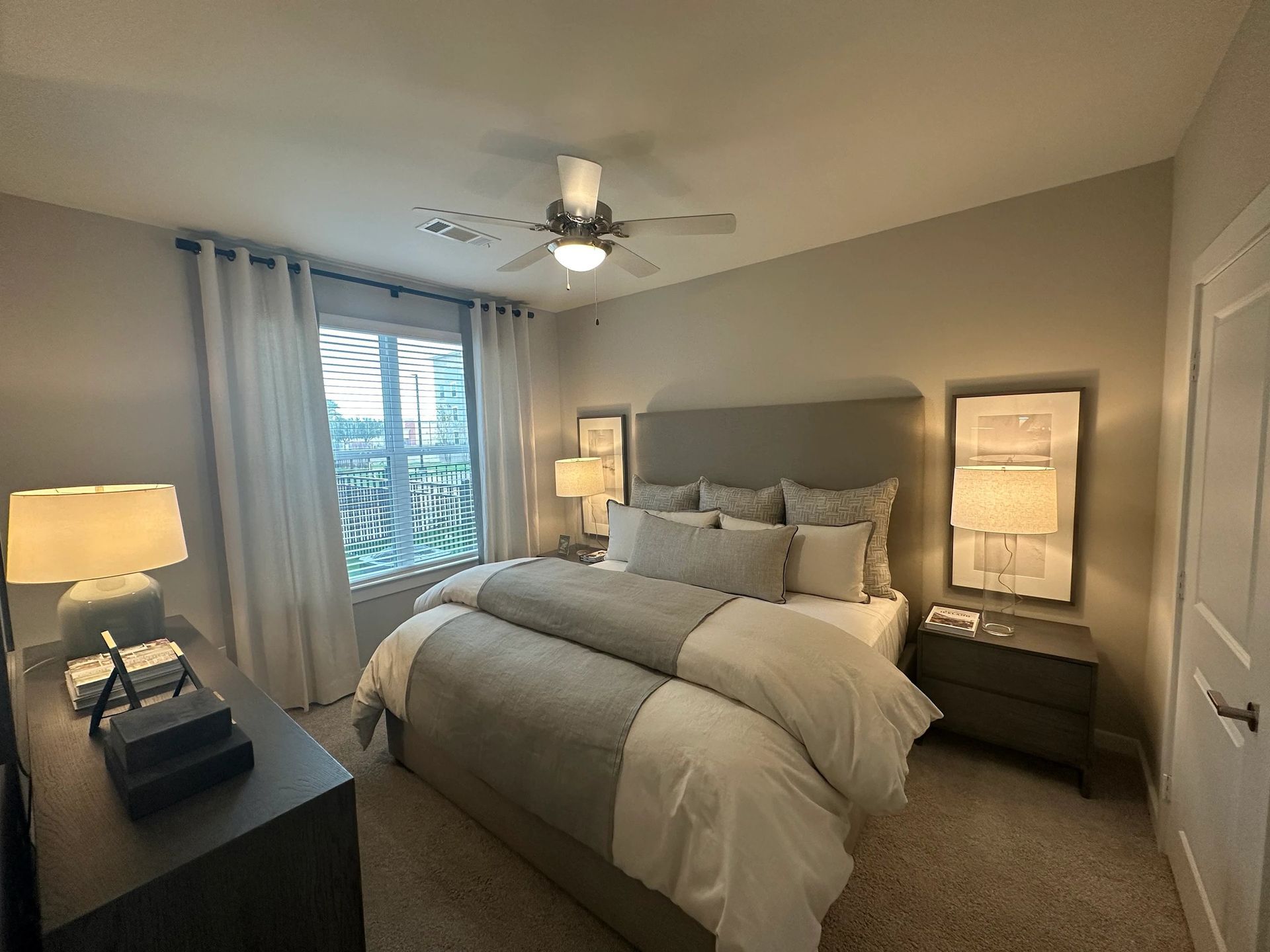 Cozy bedroom with a large bed, soft beige tones, bedside lamps, and a window with curtains.