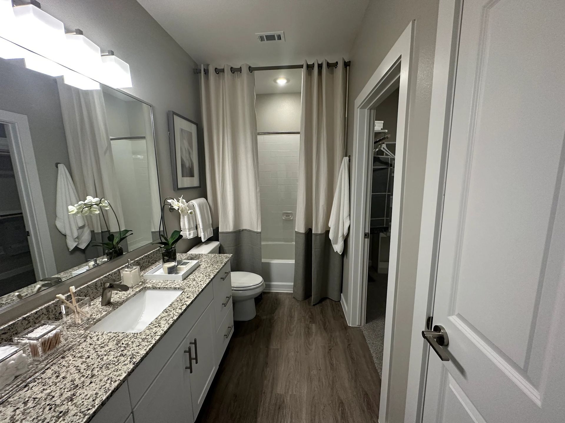 Bright bathroom with double vanity, large mirror, granite countertop, and shower curtain by the toilet.