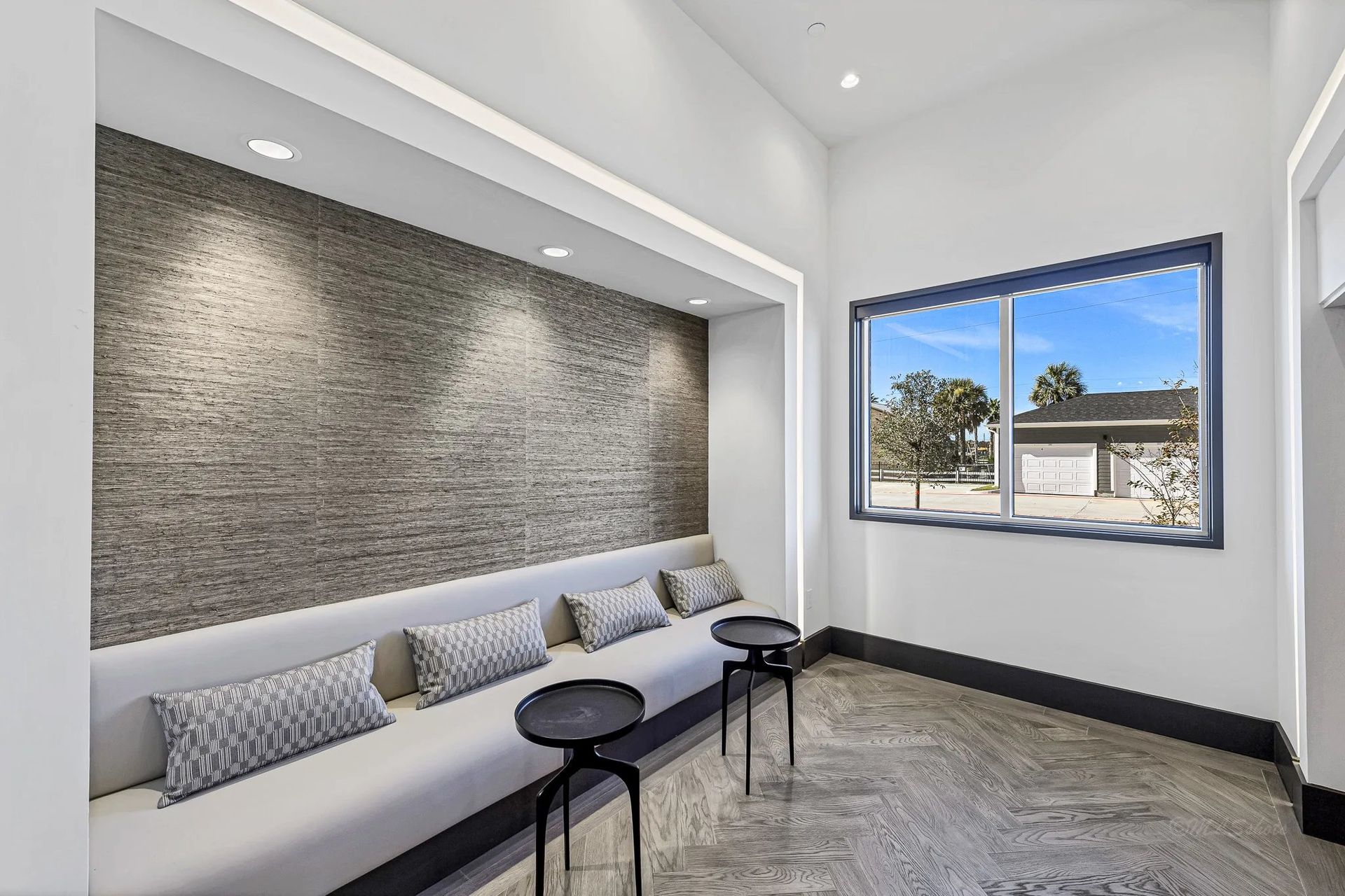 Modern waiting area with gray bench, small tables, stone accent wall, and a window to palm trees