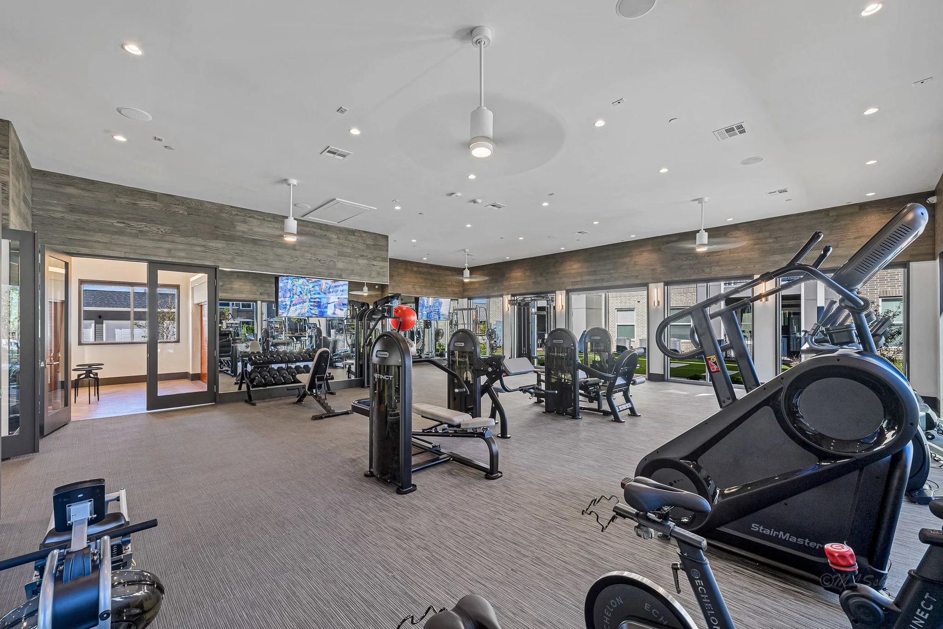 Modern gym with cardio and strength machines, mirrors, and large windows under bright lighting