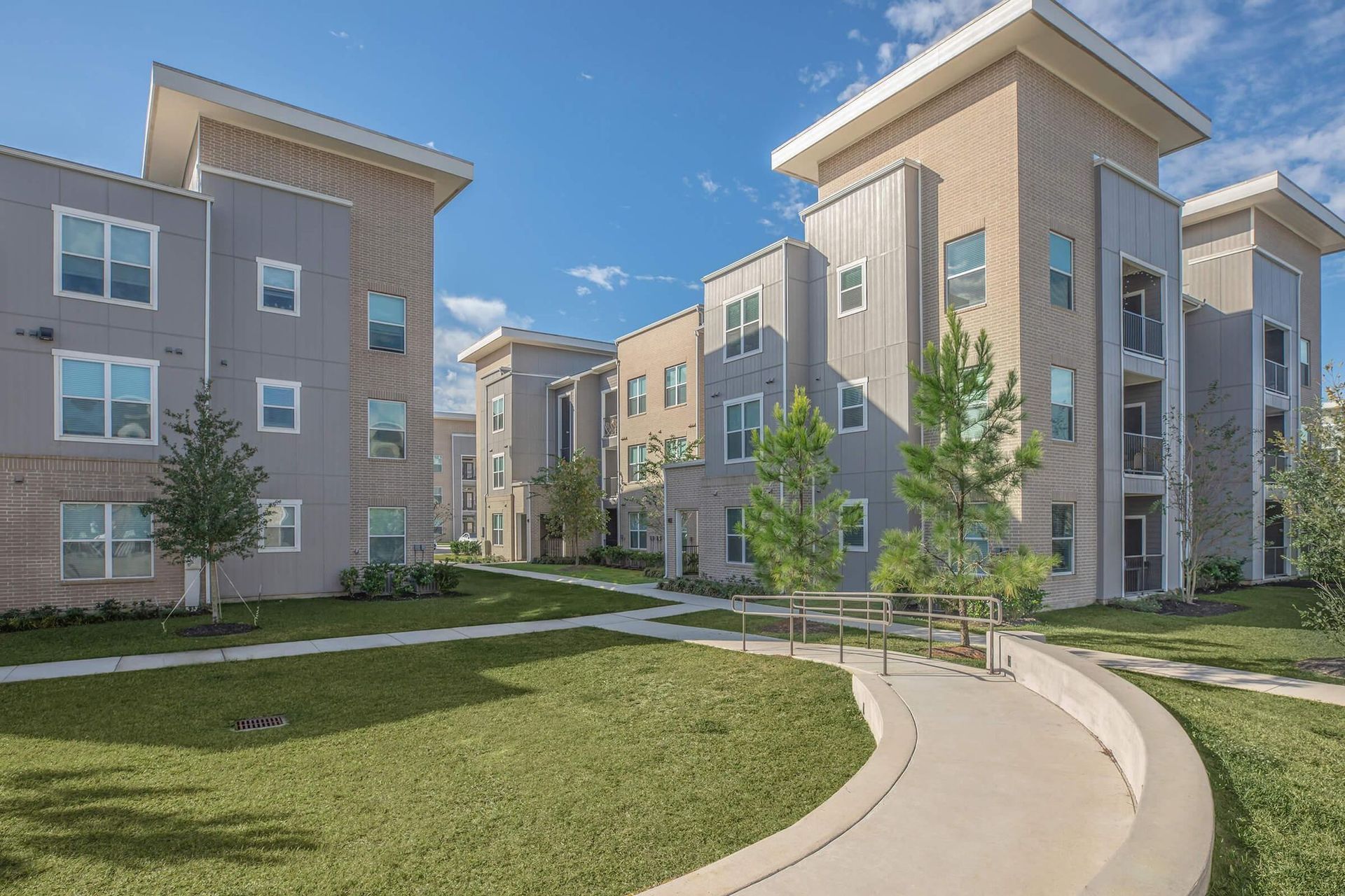 Modern apartment complex with beige buildings, green lawn, and curved walkway under a blue sky