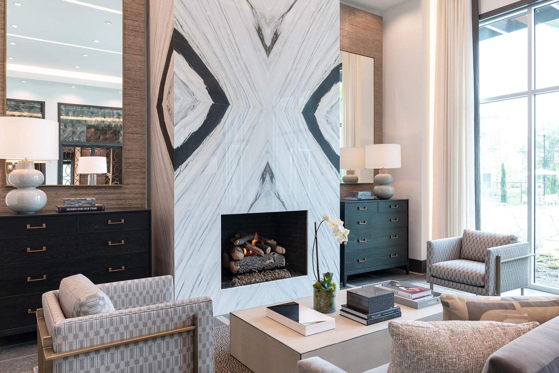 Bright living room with a marble fireplace, blue chairs, and large windows