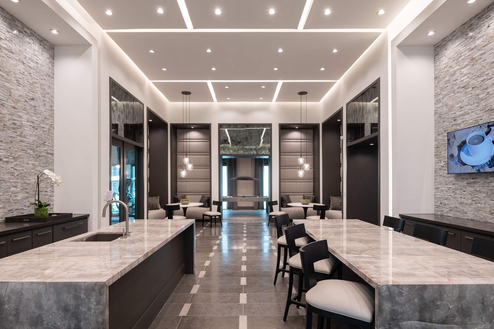 Modern hotel lounge with marble tables, dark chairs, and a bright, symmetrical ceiling design.