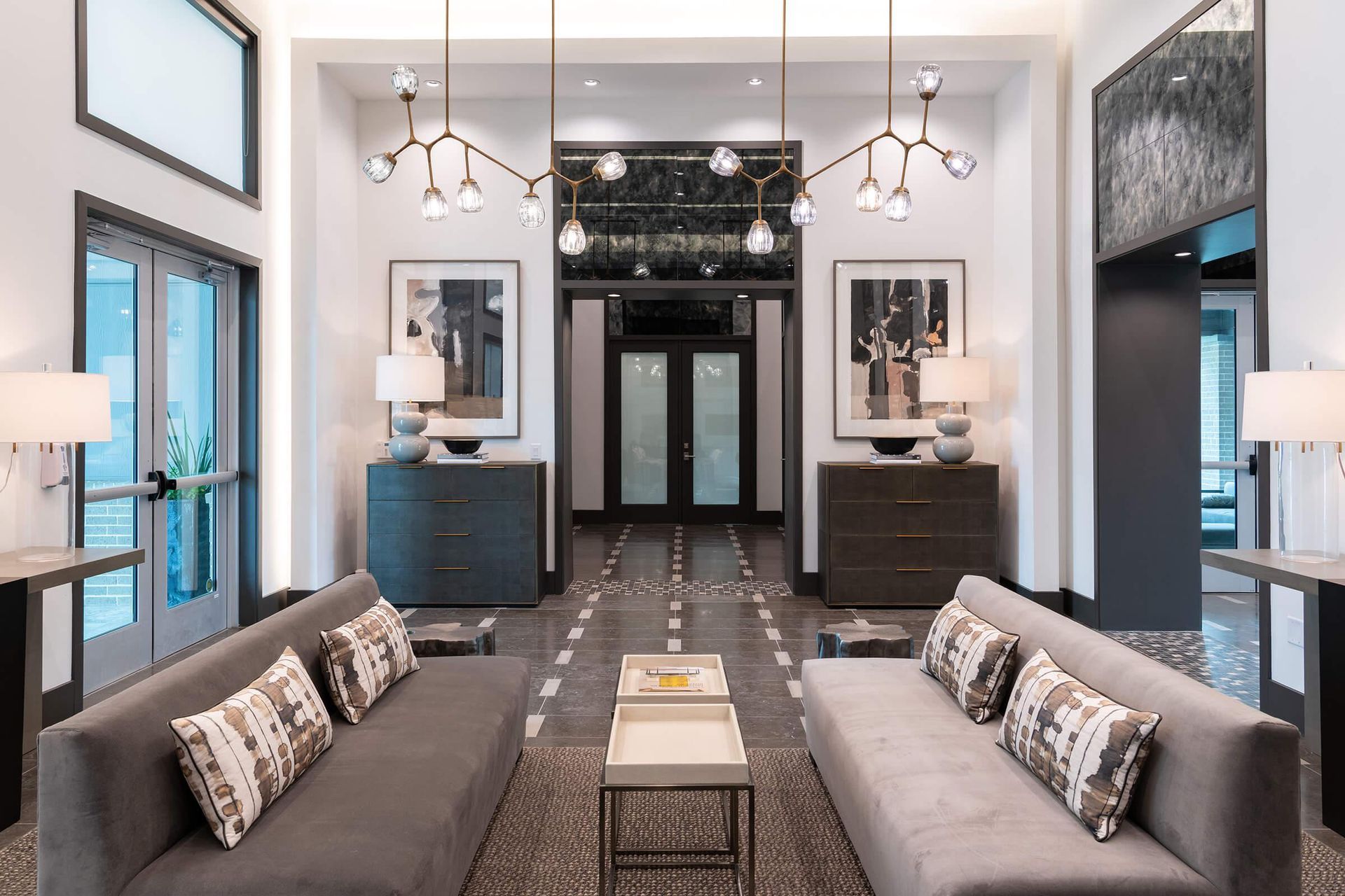 Modern hotel lobby with gray sofas, chandeliers, and a patterned black-and-white floor