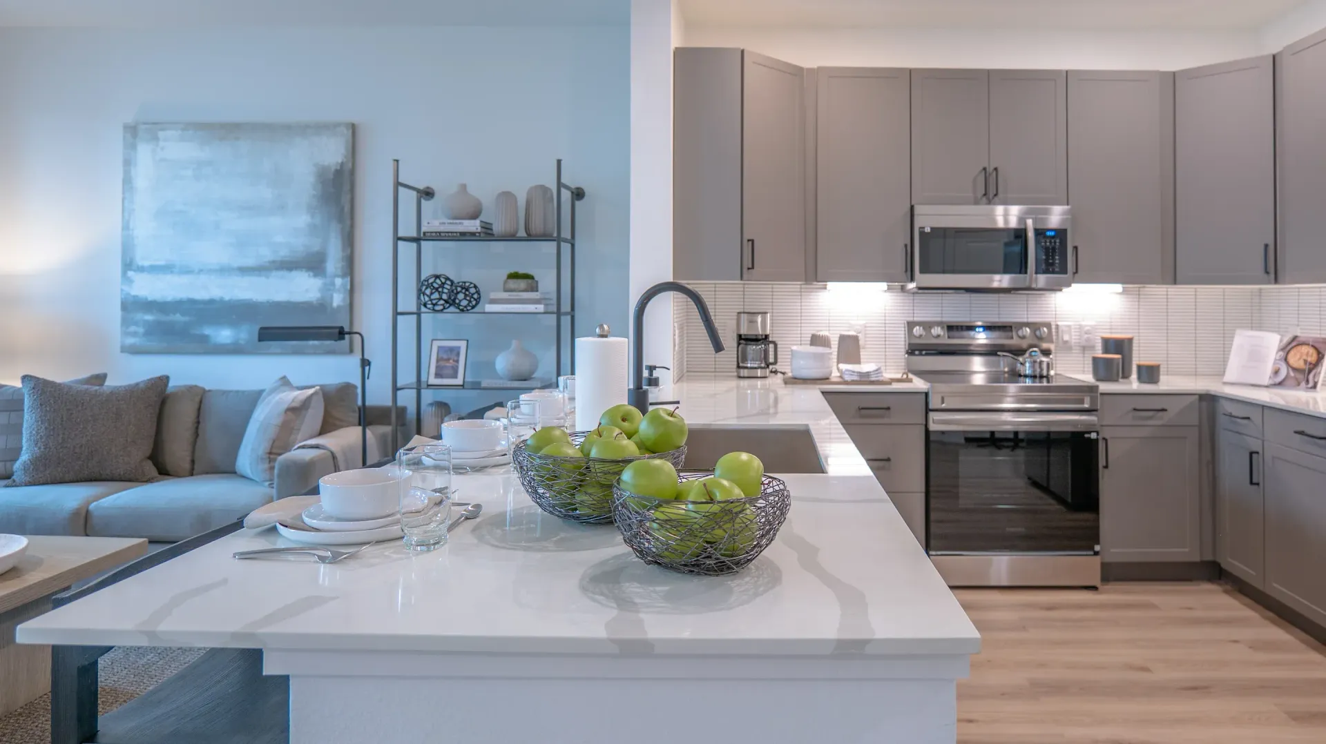 Bright modern kitchen with island, gray cabinets, and a living room with sofa and wall art.