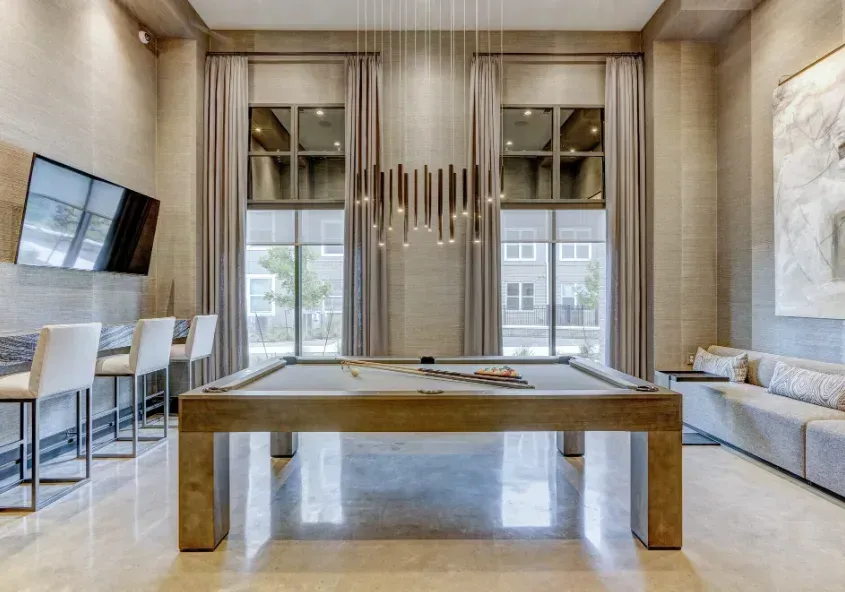 Modern lounge with a pool table, wall-mounted TV, and sofas in a bright, wood-paneled room