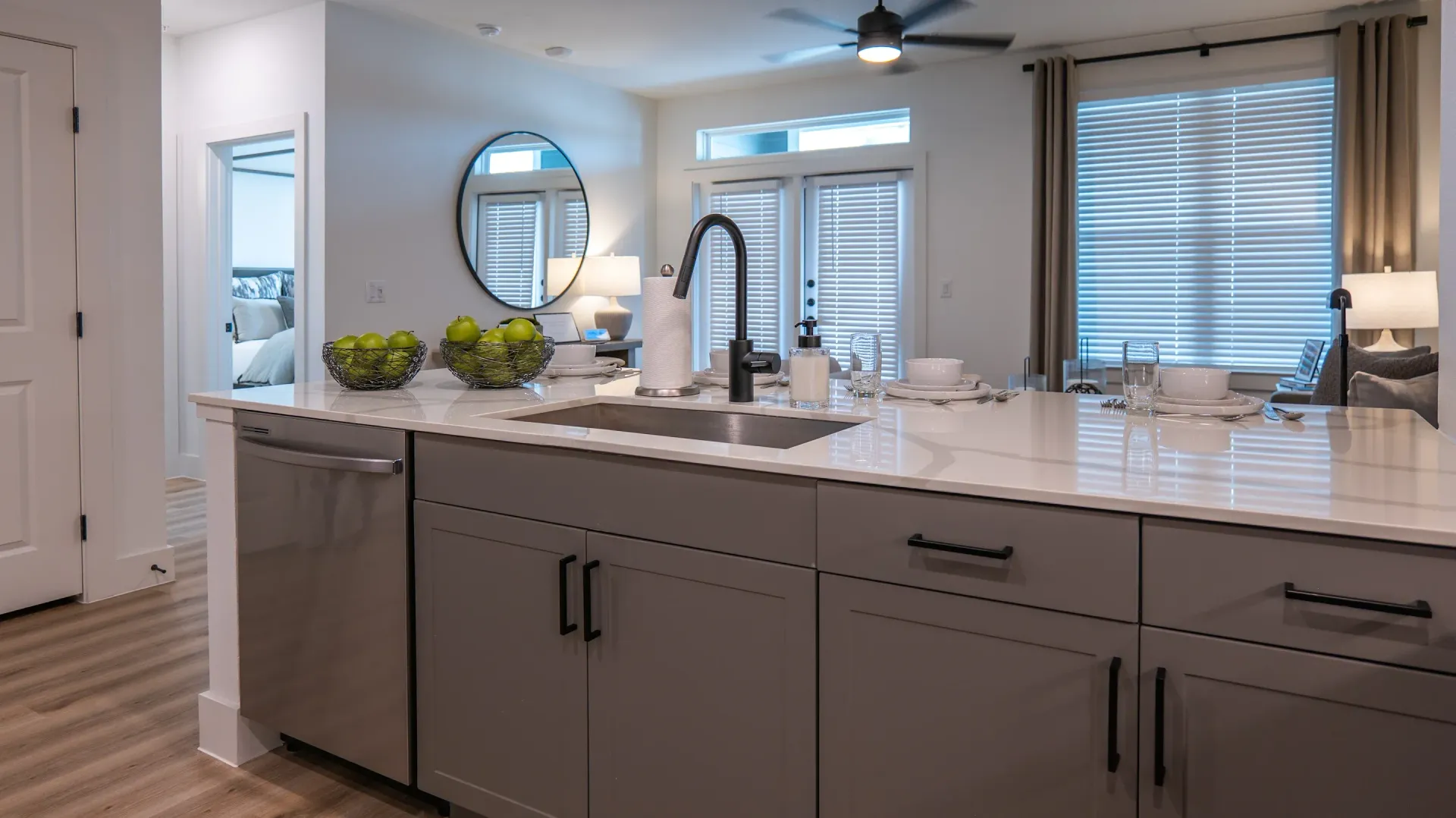 Bright modern kitchen with white cabinets, gray island, and large windows with blinds