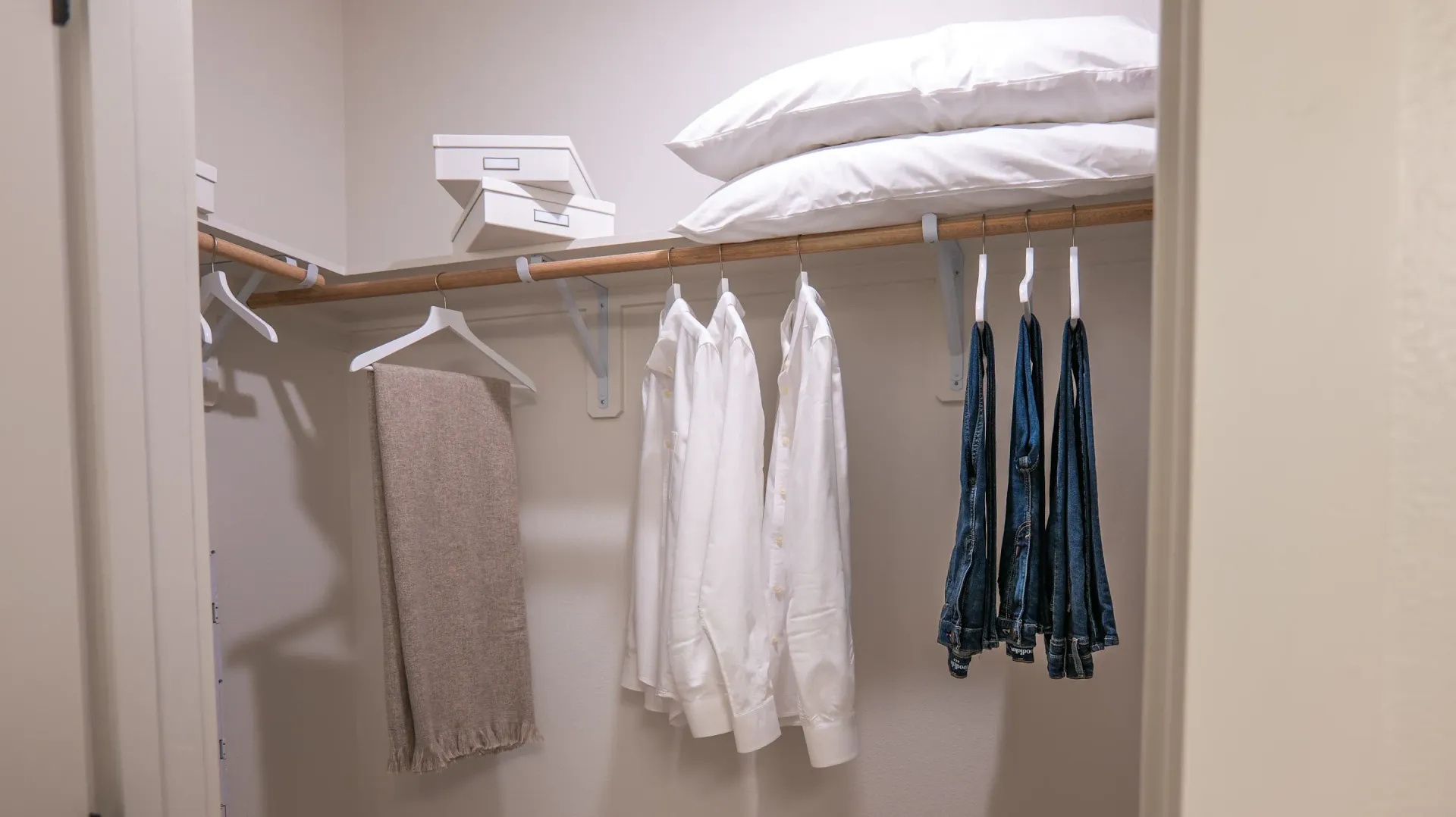 Open closet with hanging clothes and folded linens on a shelf