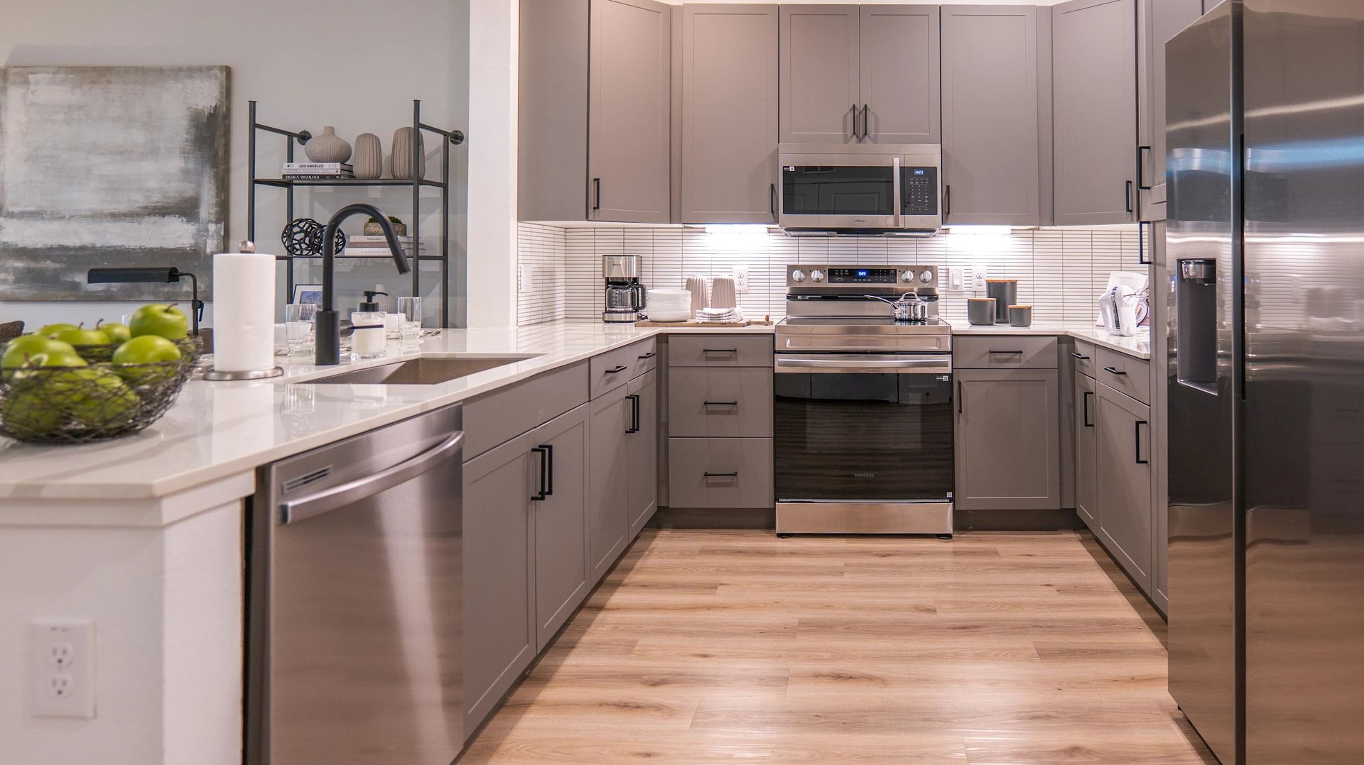 Modern kitchen with gray cabinets, stainless steel appliances, white countertops, and wood flooring