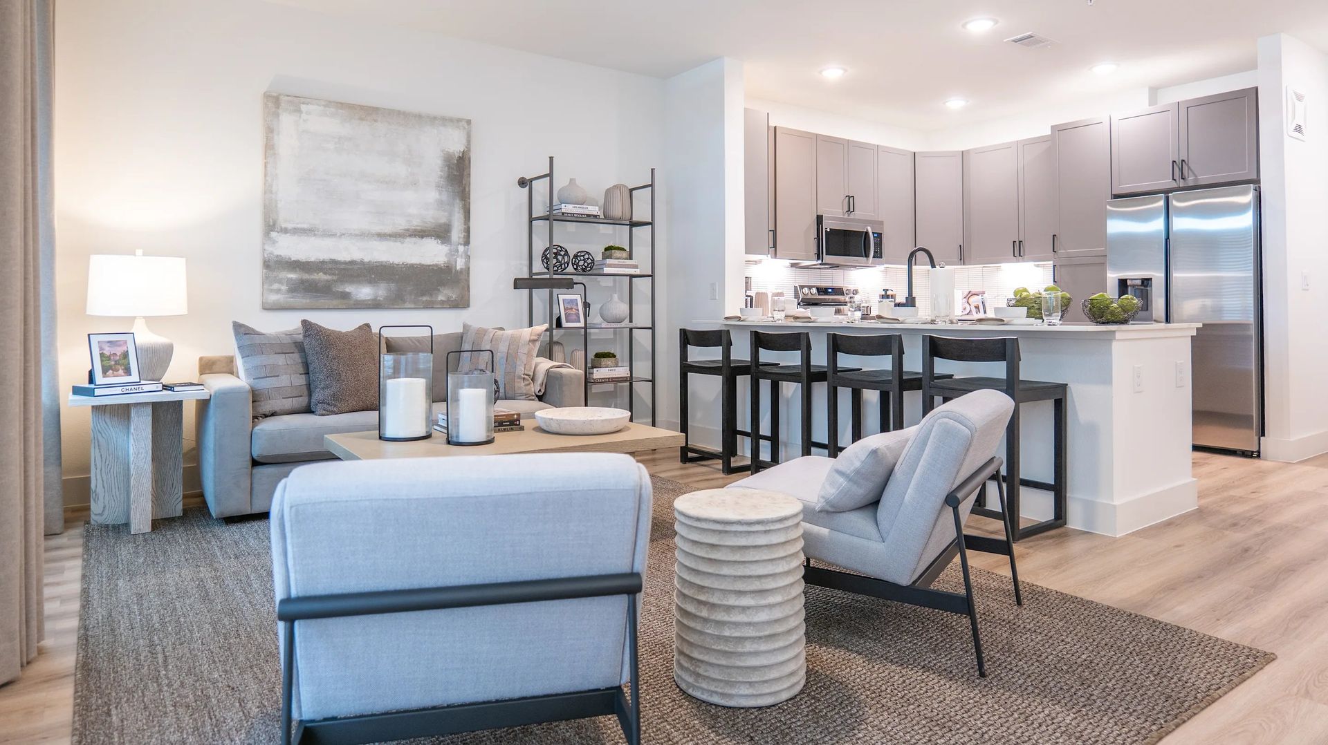 Bright modern living room with gray sofa, armchairs, kitchen island, and stainless steel appliances