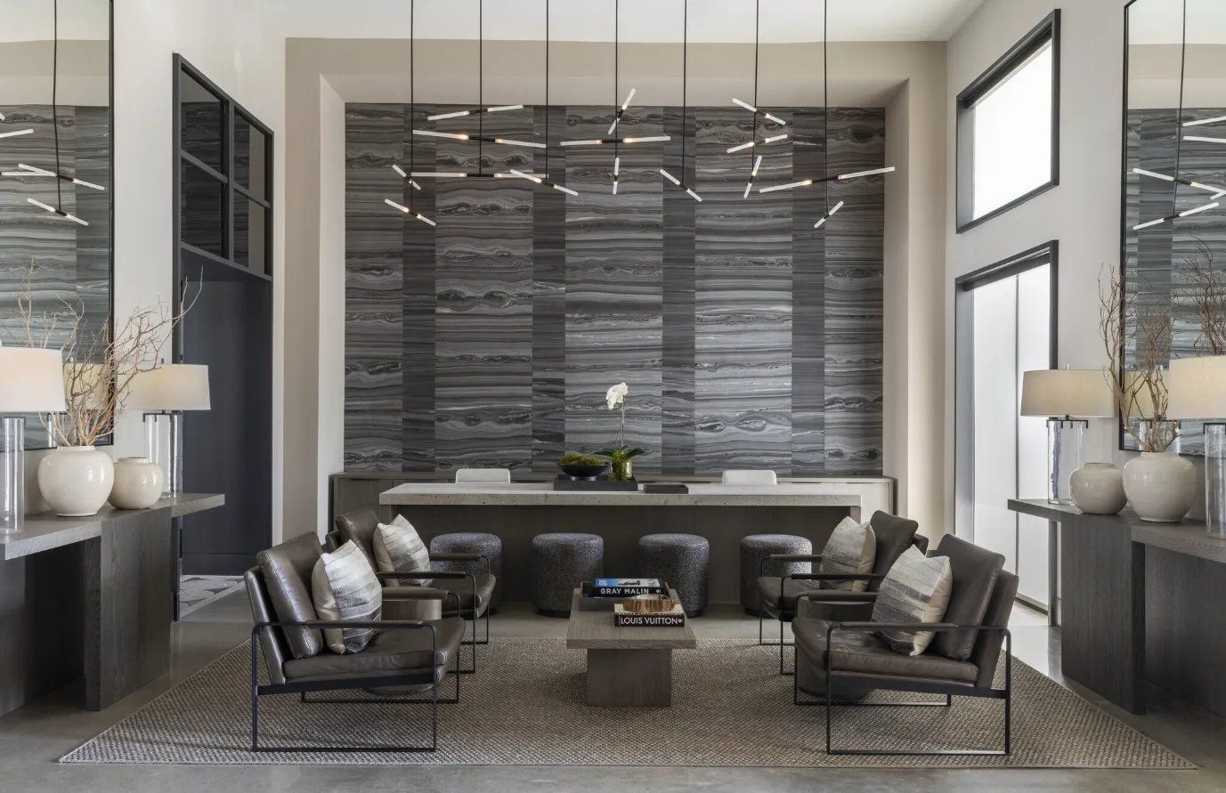Modern hotel lobby with gray seating, marble walls, pendant lights, and a sleek fireplace-like centerpiece