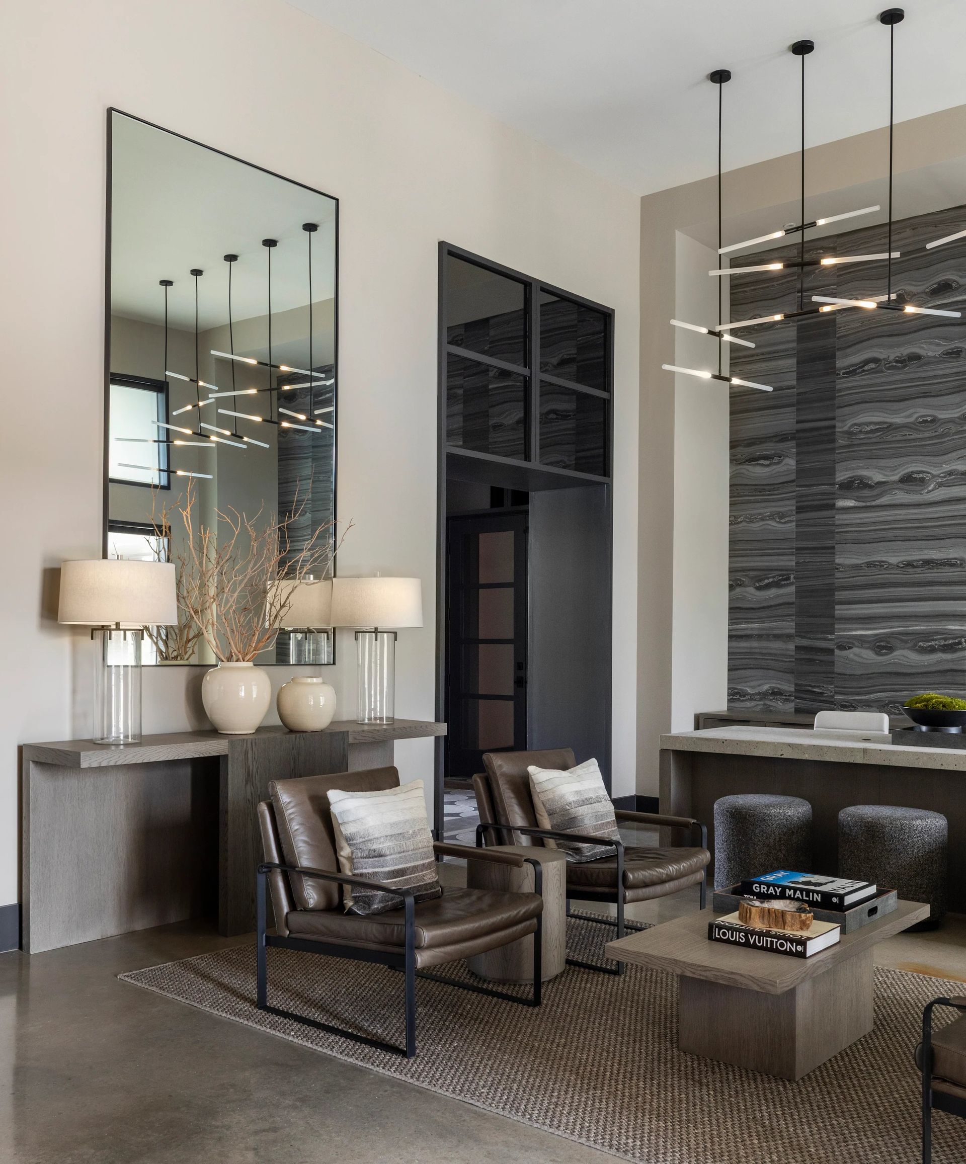 Modern living room with tall mirror, lamps, leather chairs, sectional sofa, and stone fireplace details
