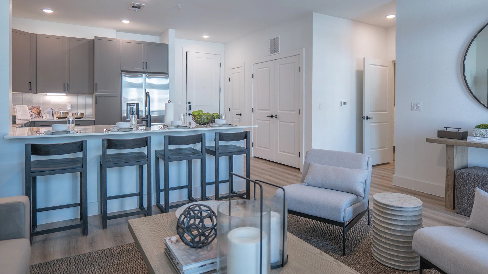 Bright modern kitchen and living area with blue bar stools, white cabinets, and light gray seating