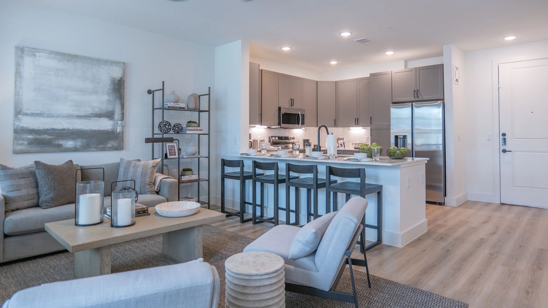 Bright modern living room with gray sofa, coffee table, and open kitchen with bar stools and stainless appliances