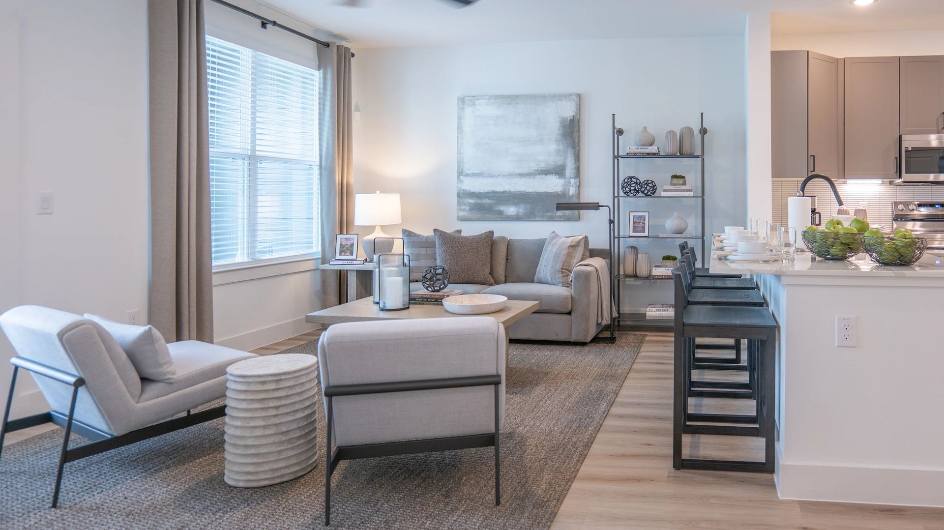 Bright modern living room with gray furniture, large window, lamp, and kitchen island with stools