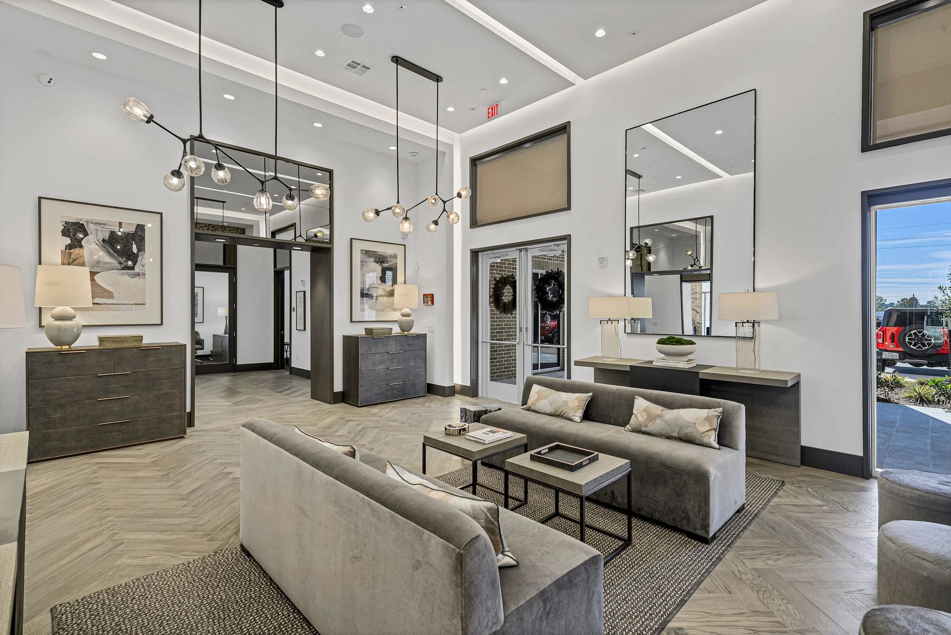 Modern luxury living room with gray sofas, large mirrors, pendant lights, and an open foyer view