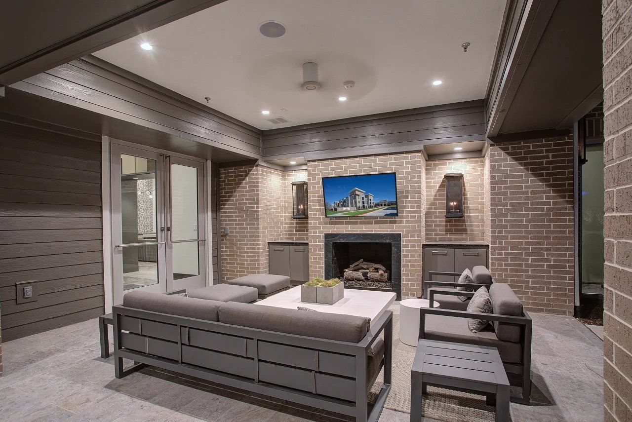Modern living room with gray sofas, brick fireplace, wall-mounted TV, and recessed lighting