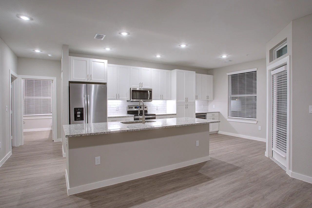 Modern white kitchen with stainless appliances, island, recessed lighting, and light wood floors