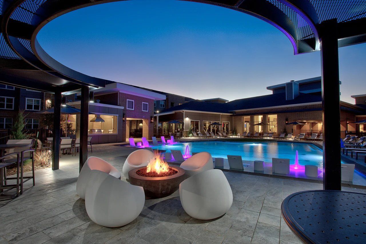 Nighttime resort courtyard with lit pool, fire pit, and lounge seating under a circular canopy.