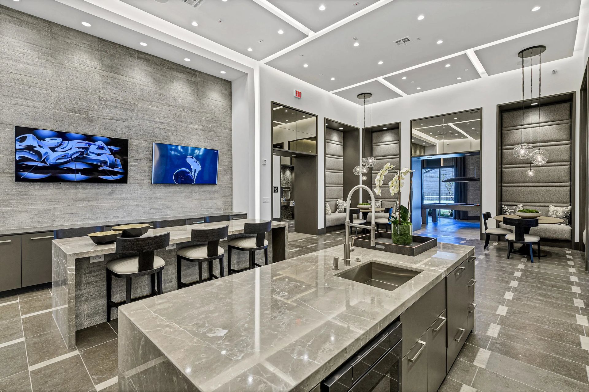 Modern luxury kitchen with marble island, bar stools, and wall-mounted TVs in a bright open living space