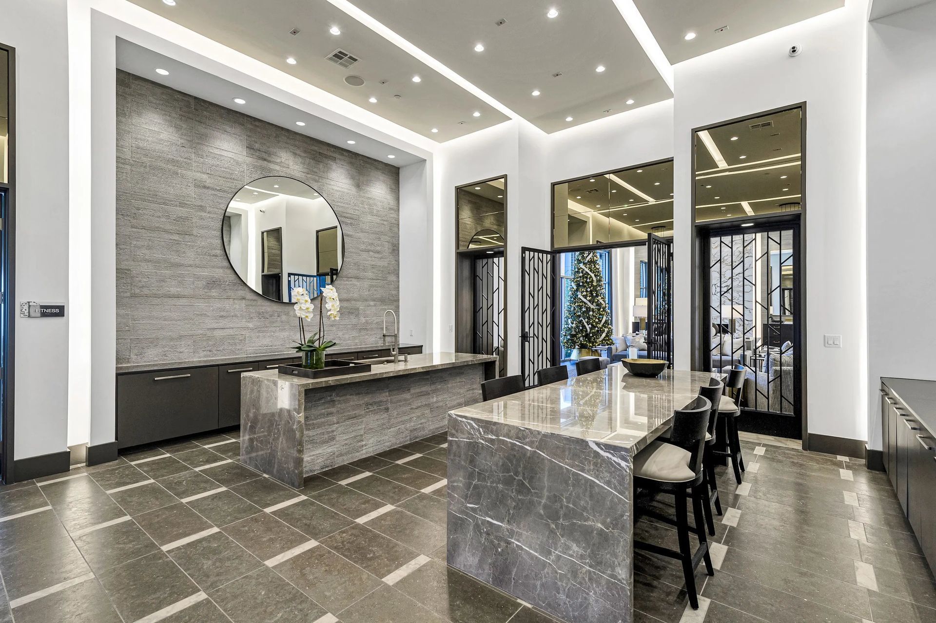 Modern luxury bathroom with gray marble counters, large mirror, and black chairs under bright recessed lighting
