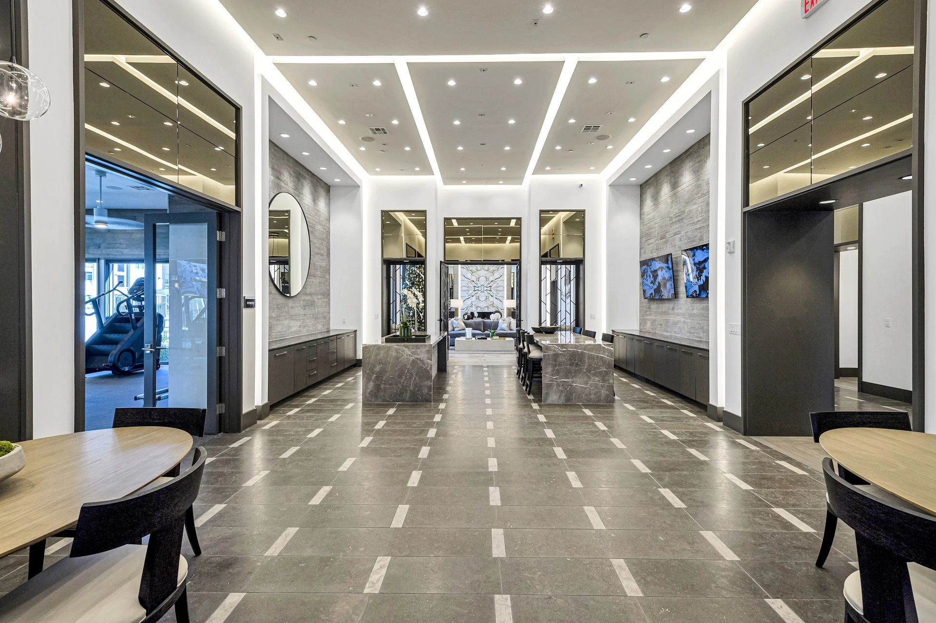 Modern lobby with polished gray floors, bright ceiling lights, and glass walls leading to seating areas