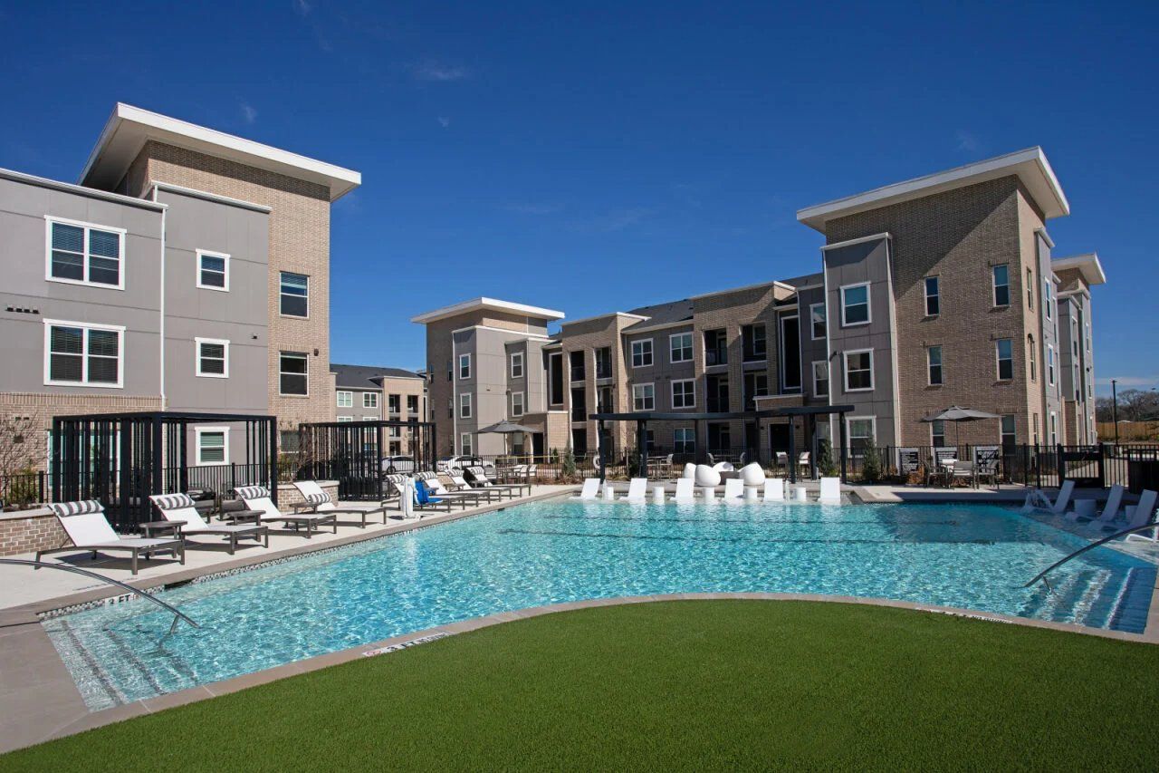 Modern apartment complex with a large outdoor swimming pool and lounge chairs on a sunny day