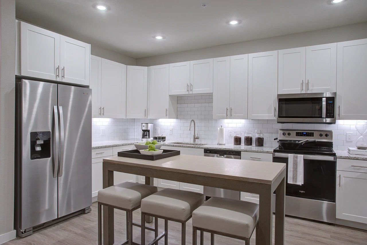 Bright modern white kitchen with stainless steel appliances, island, and four stools