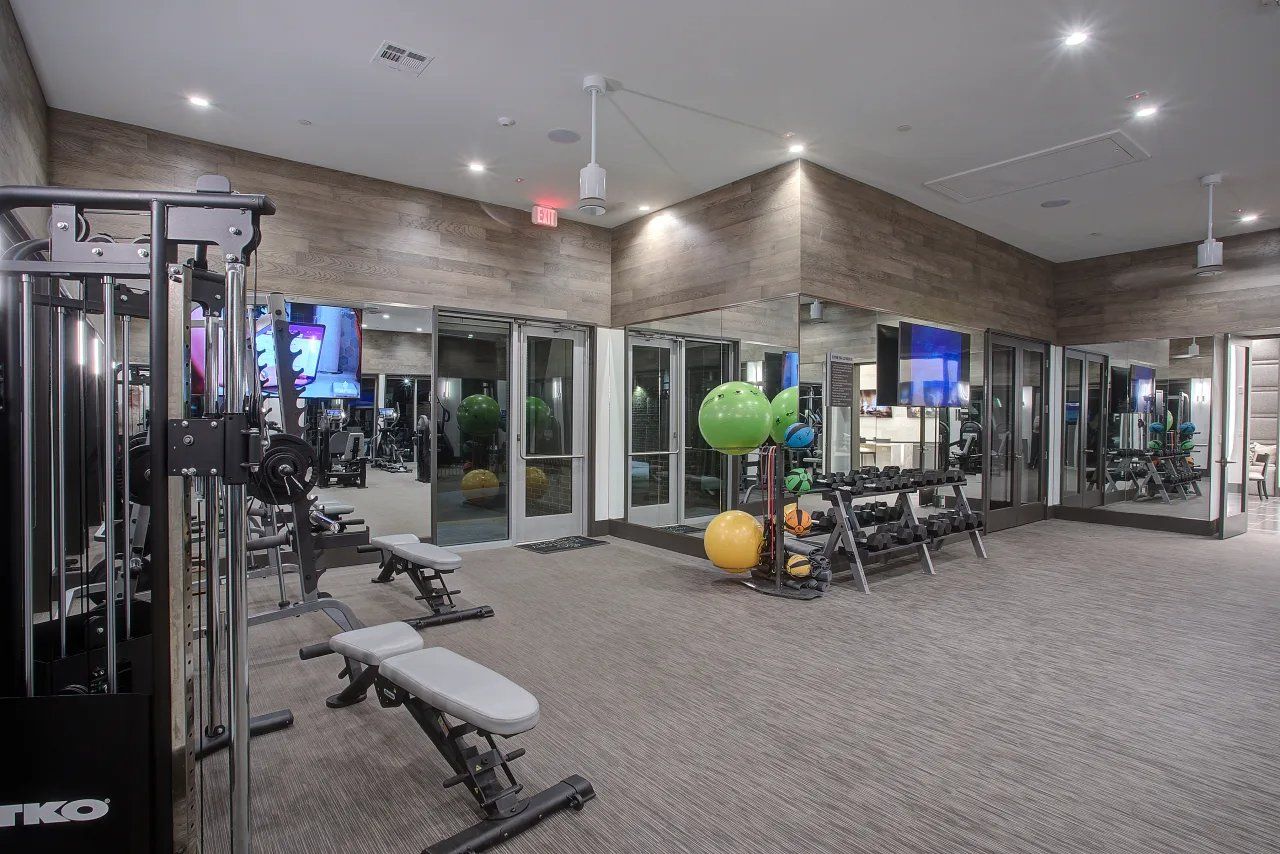 Gym interior with weight machines, benches, mirrors, and colorful exercise balls on carpeted floor