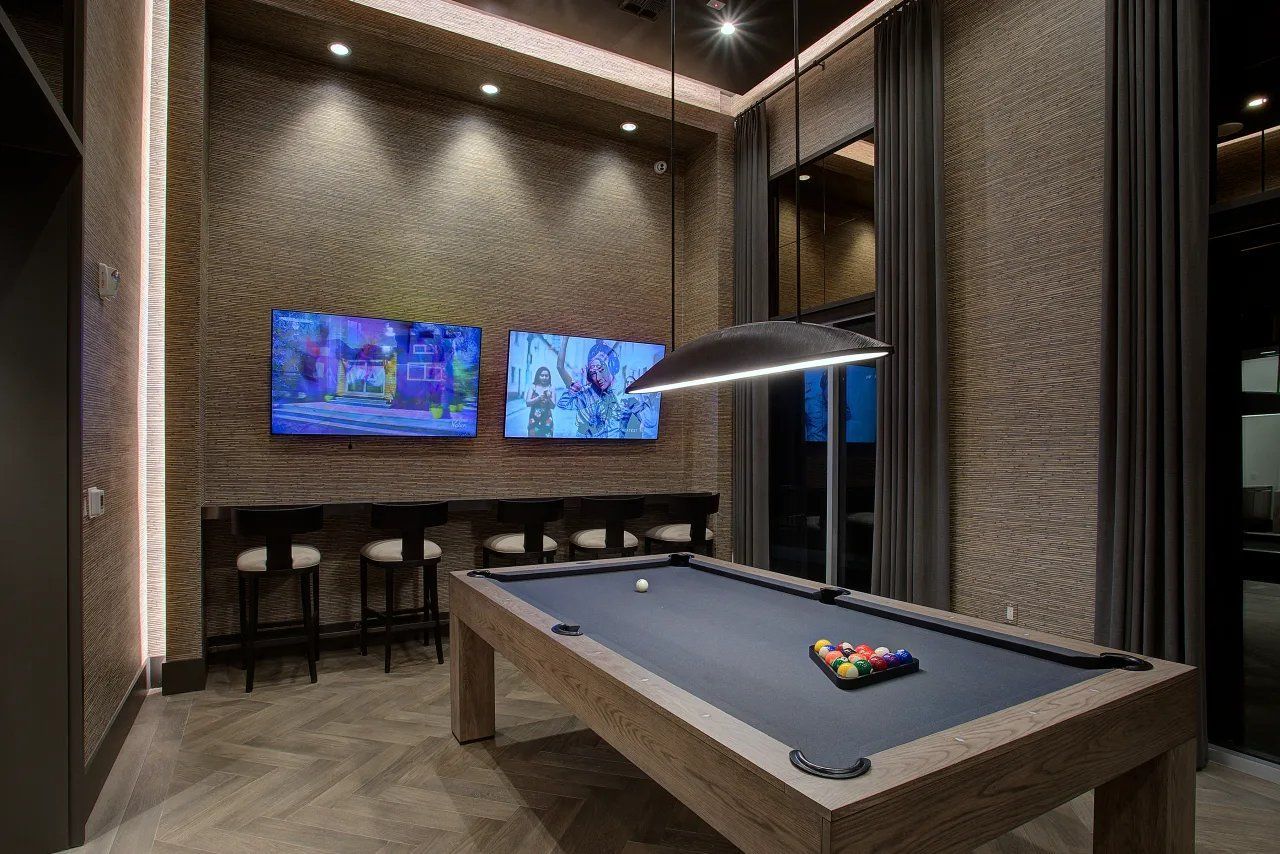 Modern game room with pool table, wall-mounted TVs, and bar seating under warm lighting