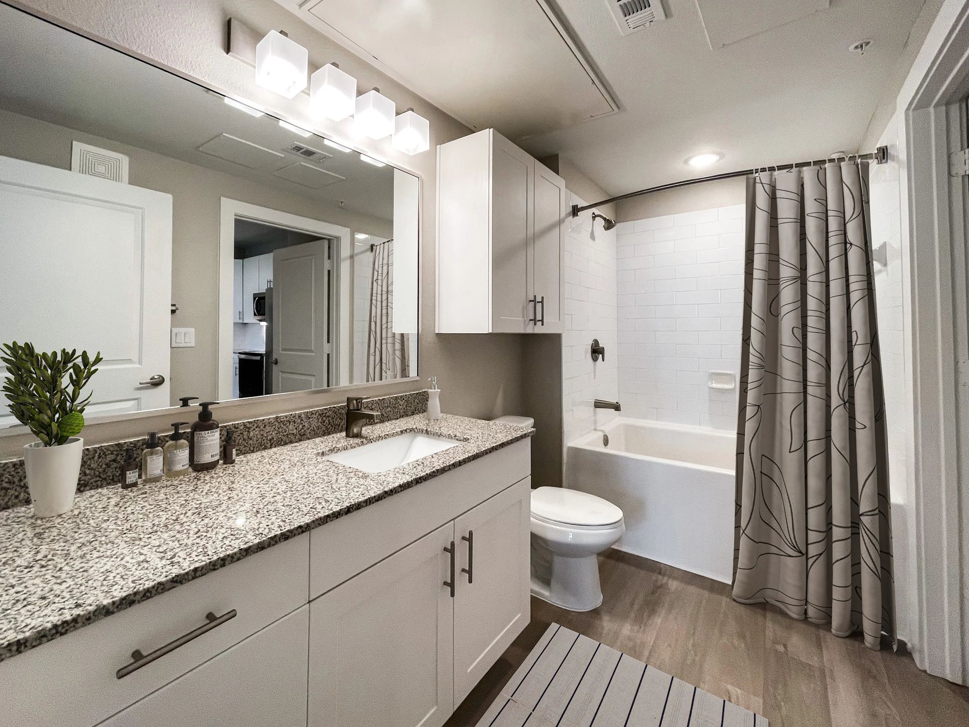 Modern bathroom with granite vanity, mirror, toilet, bathtub, and gray shower curtain.