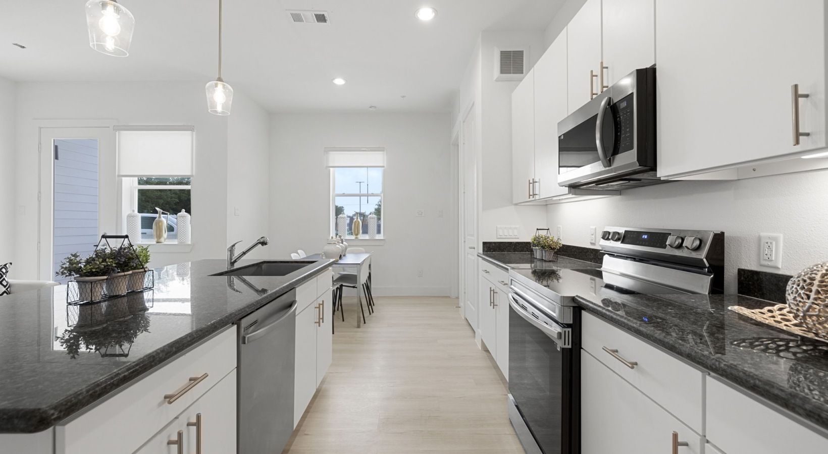 Bright modern kitchen with white cabinets, black countertops, stainless appliances, and an island with flowers.