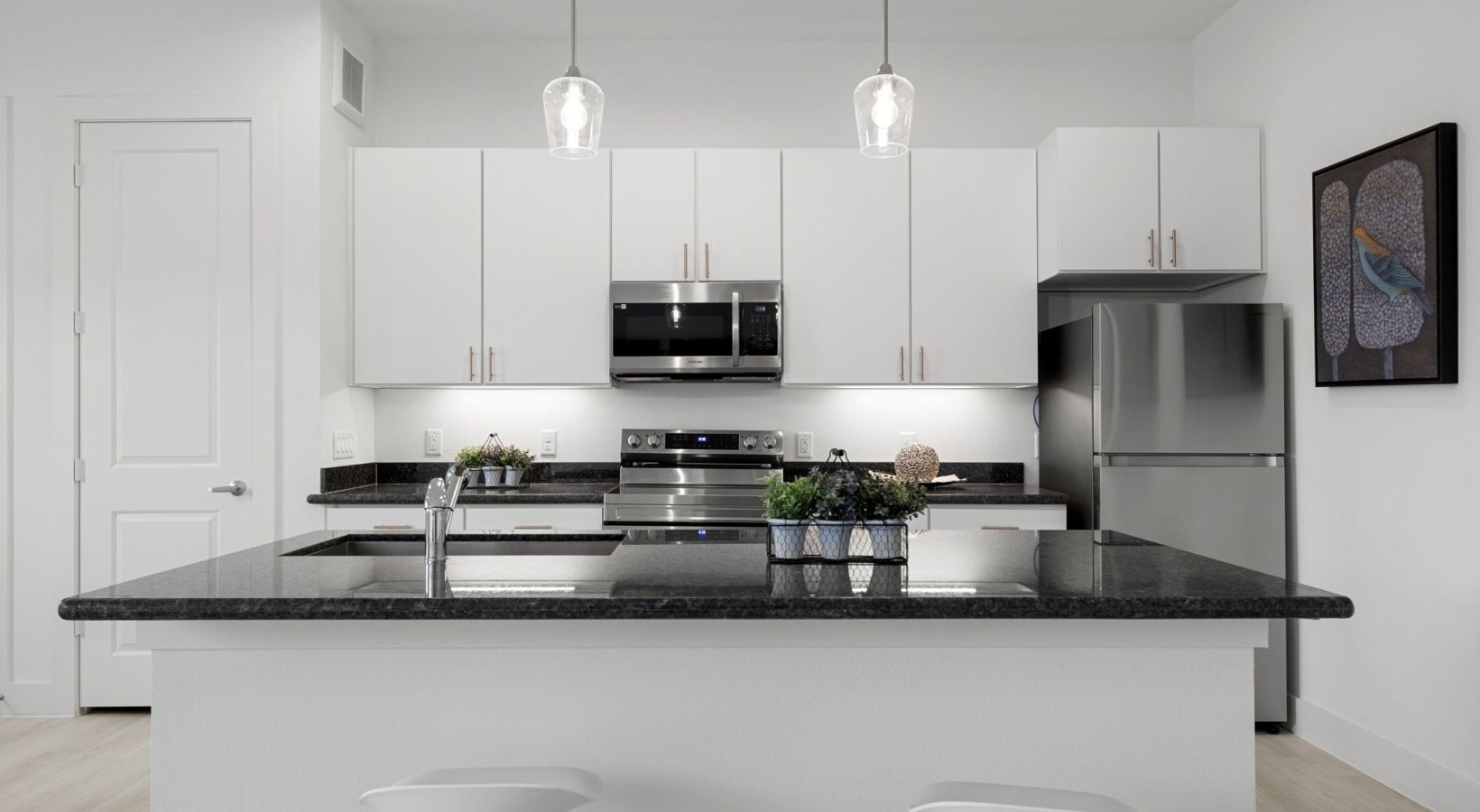Modern white kitchen with large black island, stainless appliances, and pendant light