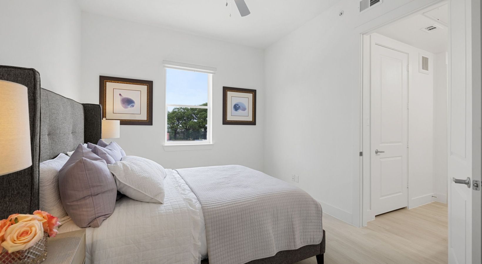 Bright white bedroom with a gray headboard, bed, two framed pictures, and an open closet door.