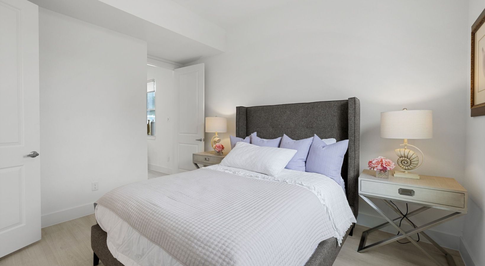 Bright white bedroom with a neatly made bed, bedside lamps, and mirrored nightstands