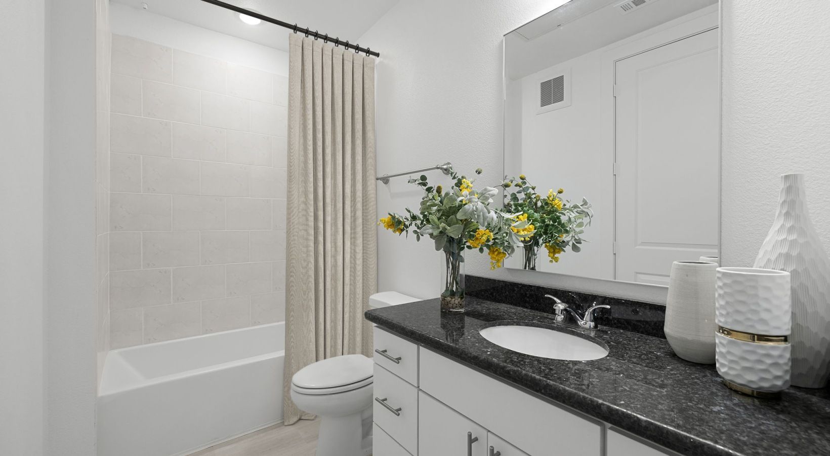 Bright bathroom with bathtub, shower curtain, vanity sink, and countertop decor.